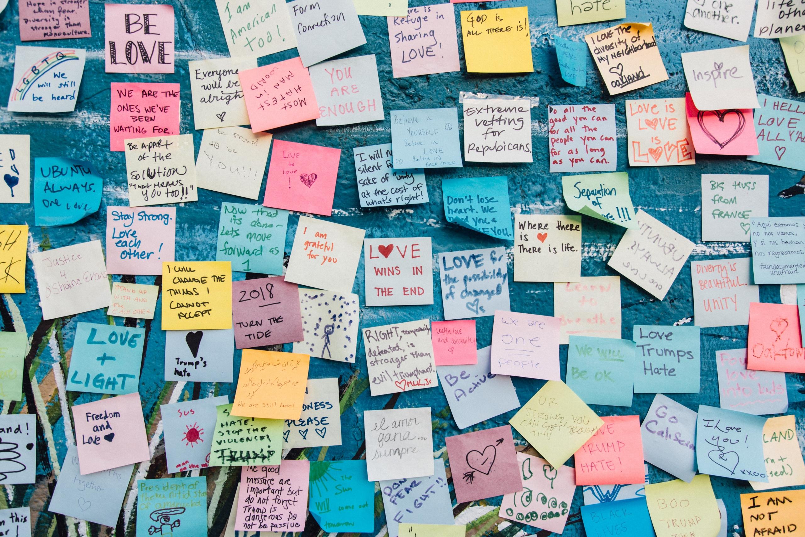 Erivärisiä postit-lappuja sinisellä seinällä.