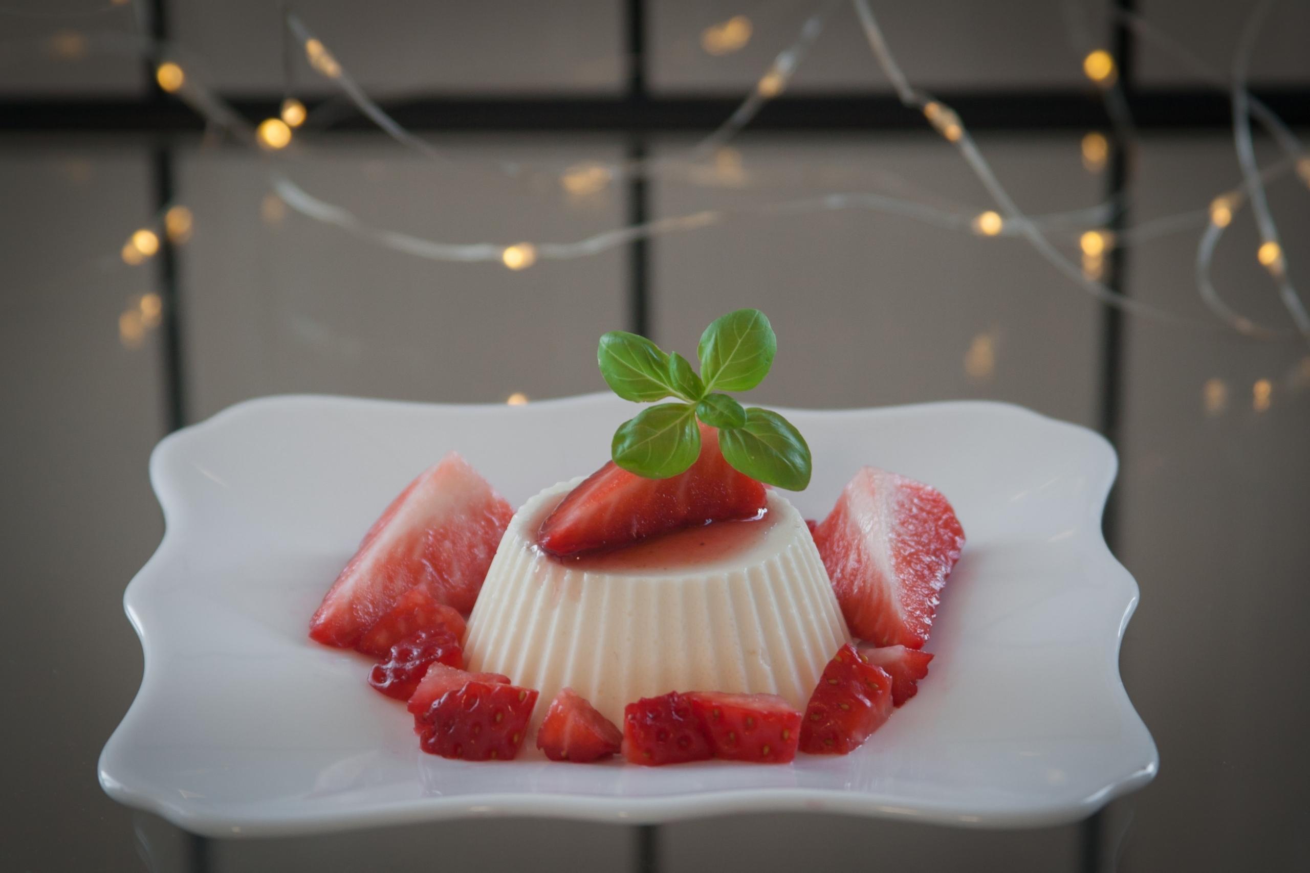 Panna cotta -jälkiruoka lautasella mansikoiden kera