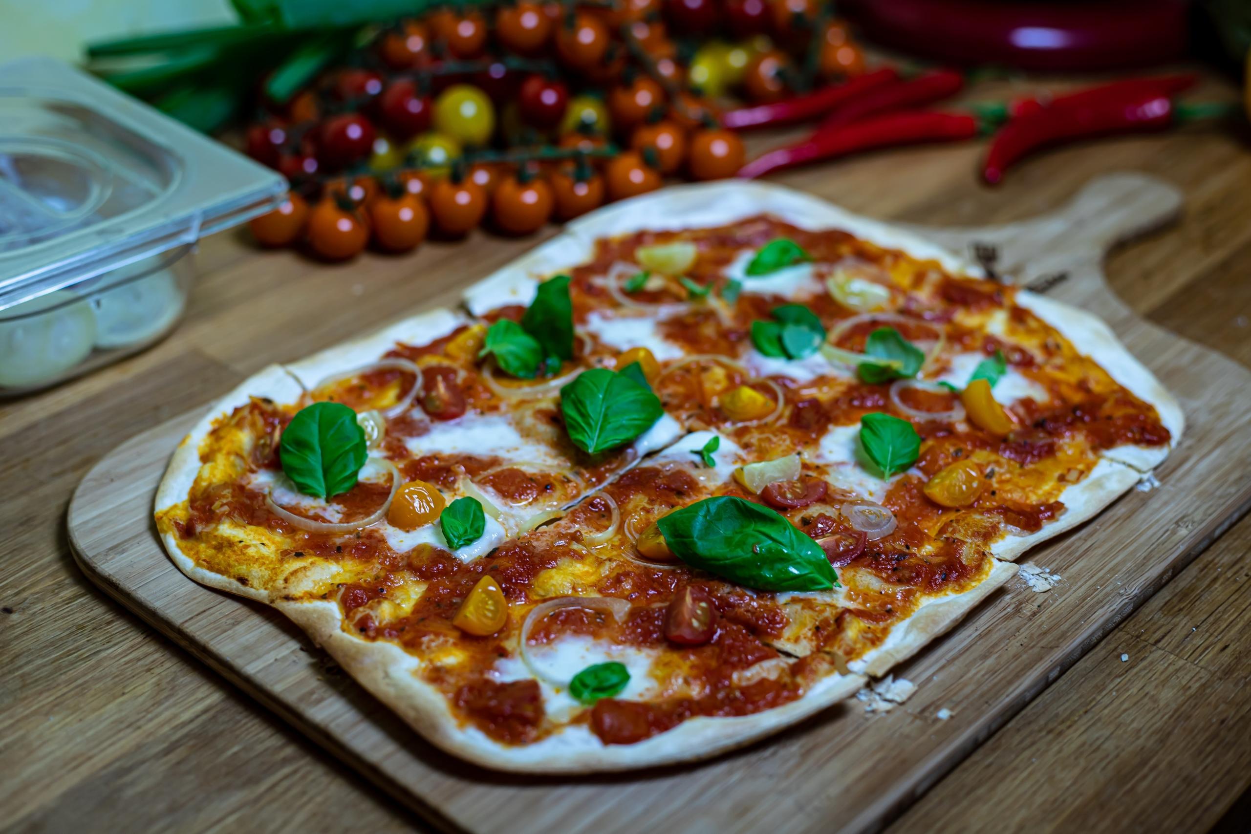 Italialainen pizza, jonka päällä kirsikkatomaatteja, tomaattikastiketta, bsailikaa ja sipulia