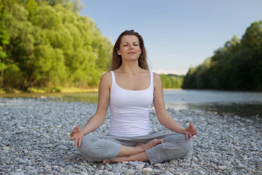 Nainen meditoimassa kivisessä maassa veden äärellä