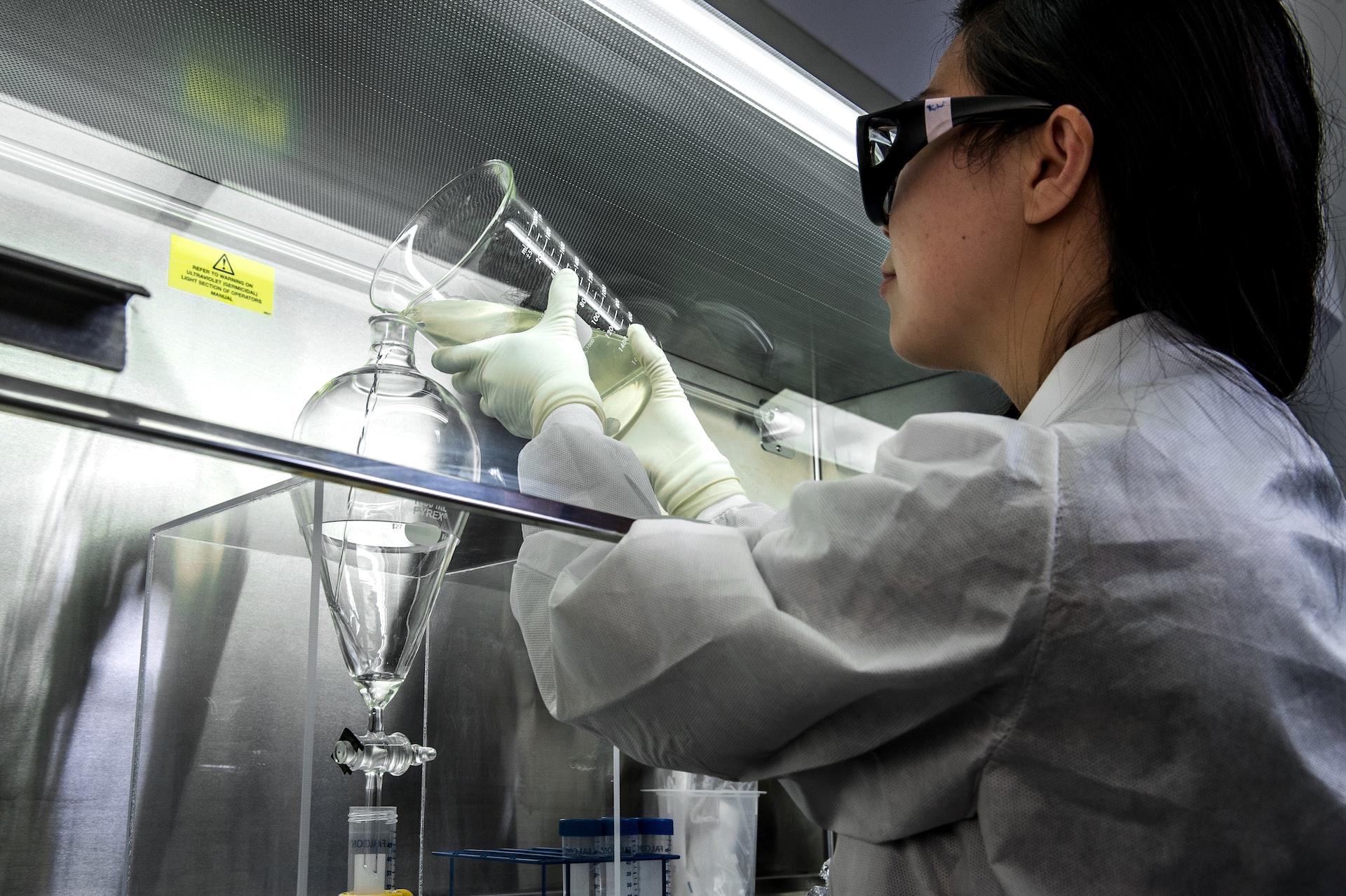 Laboratorioasuinen tutkija kaatamassa nestettä mitta-astiasta toiseen