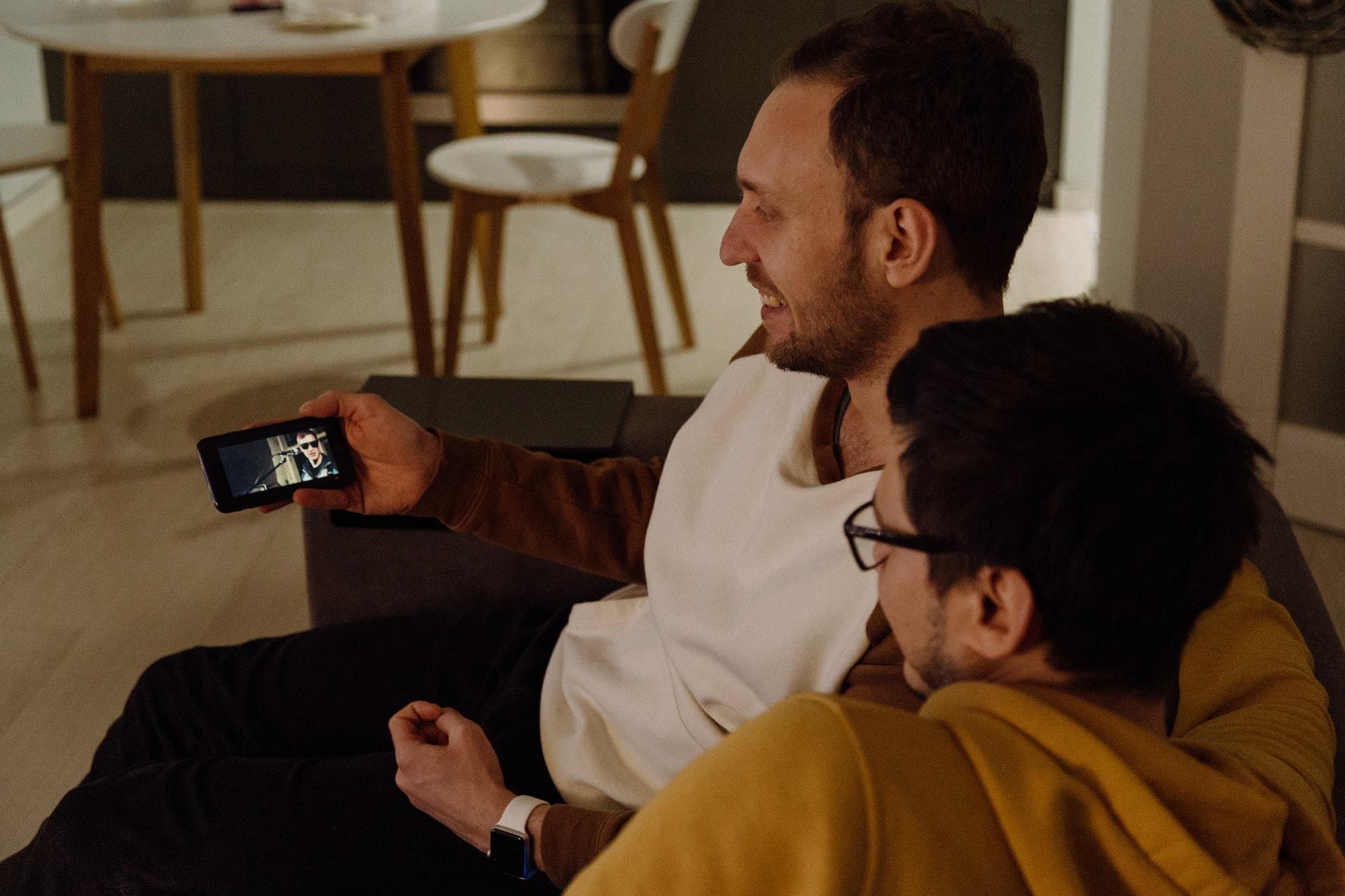 Kaksi henkilöä sohvalla katsomassa videota puhelin näytöltä