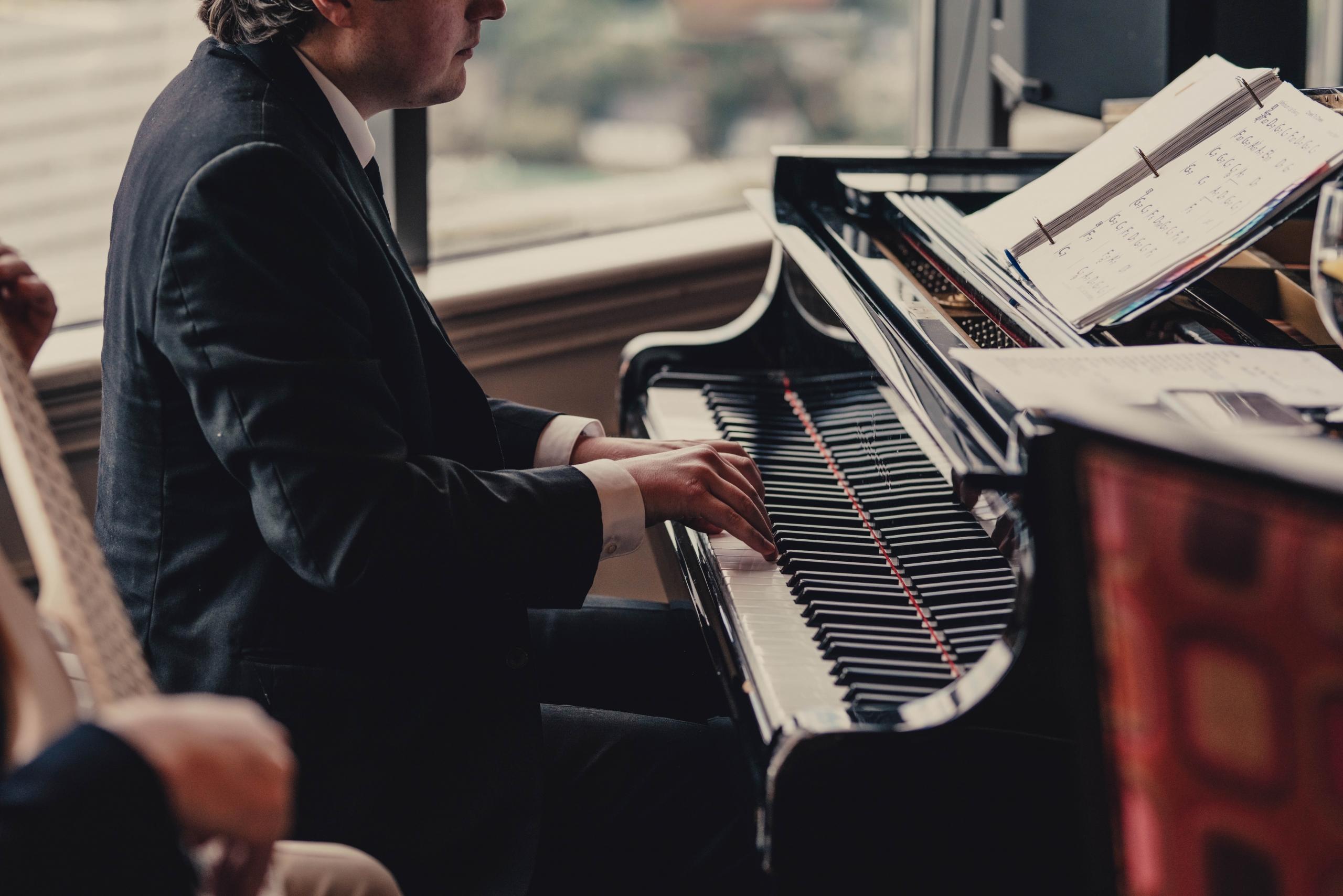 Mies soittamassa puku päällä pianoa