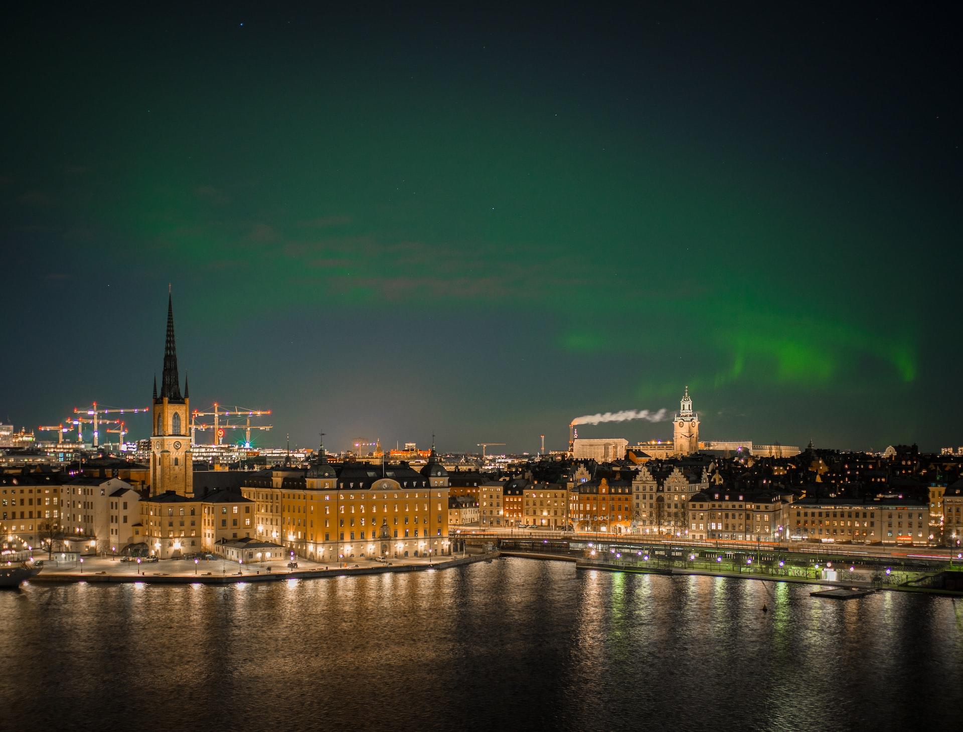 Tukholman kaupunkimaisemaa iltavalaistuksessa yllään revontulia tummalla taivaalla