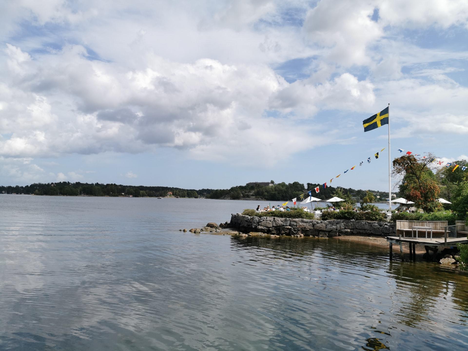 Ihmisiä istumassa rannalla, jolla myös Ruotsin lippu salossa
