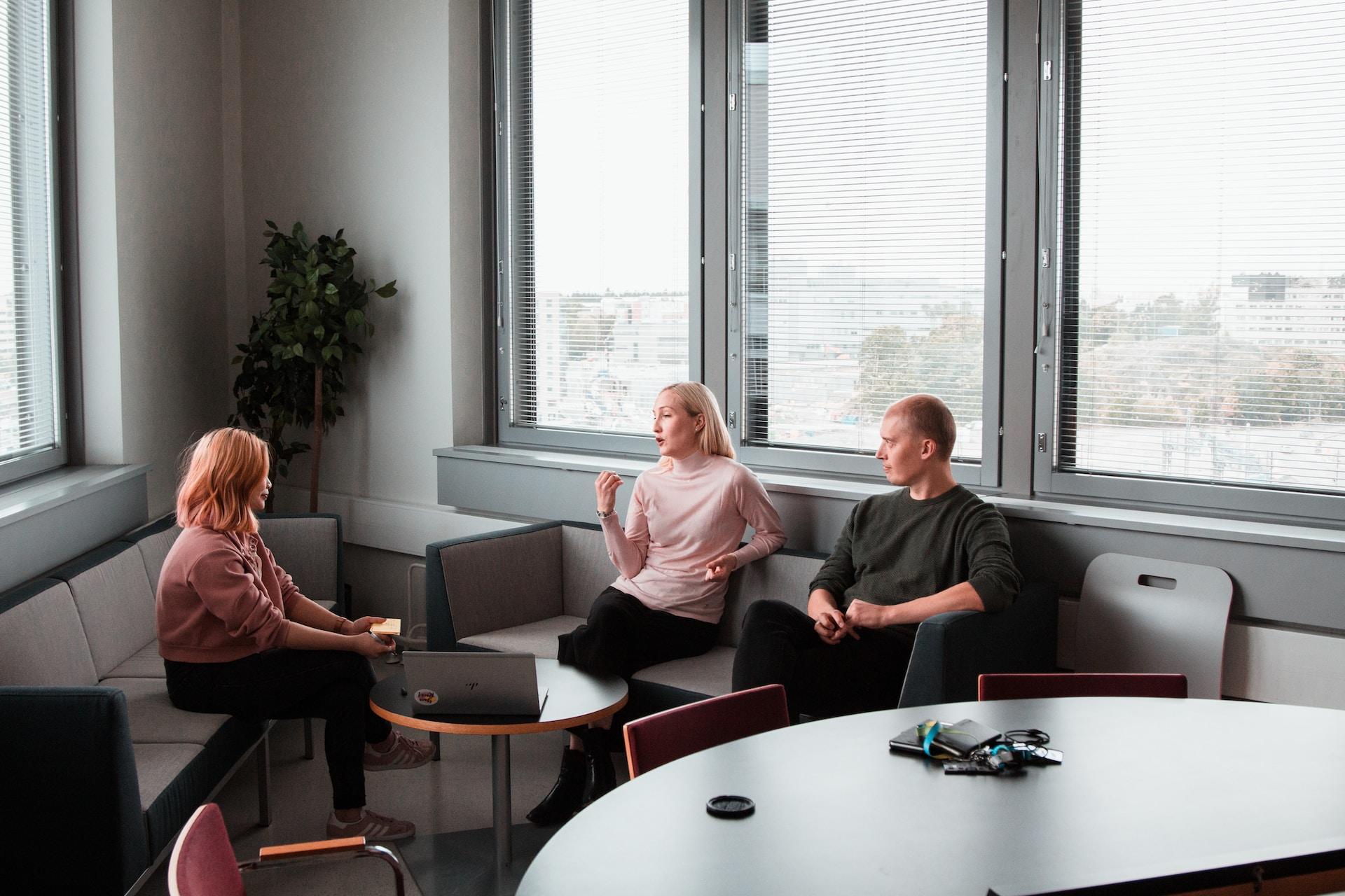 Kolme henkilöä keskustelemassa sohvilla istuen