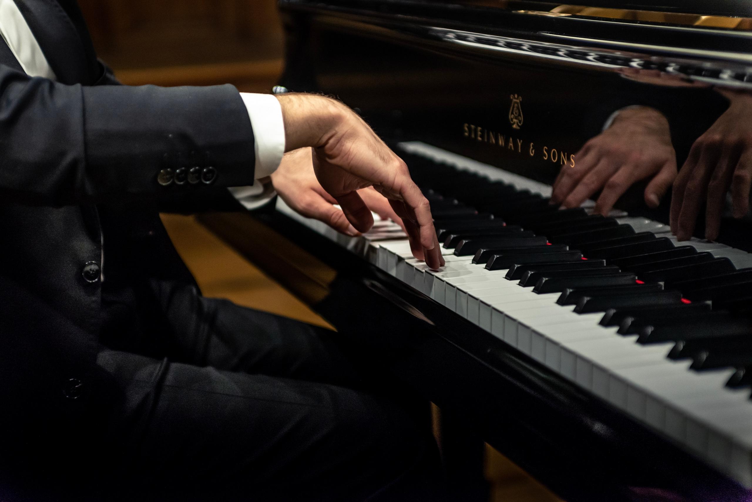 Henkilö soittamassa tummaa pianoa puku päällä