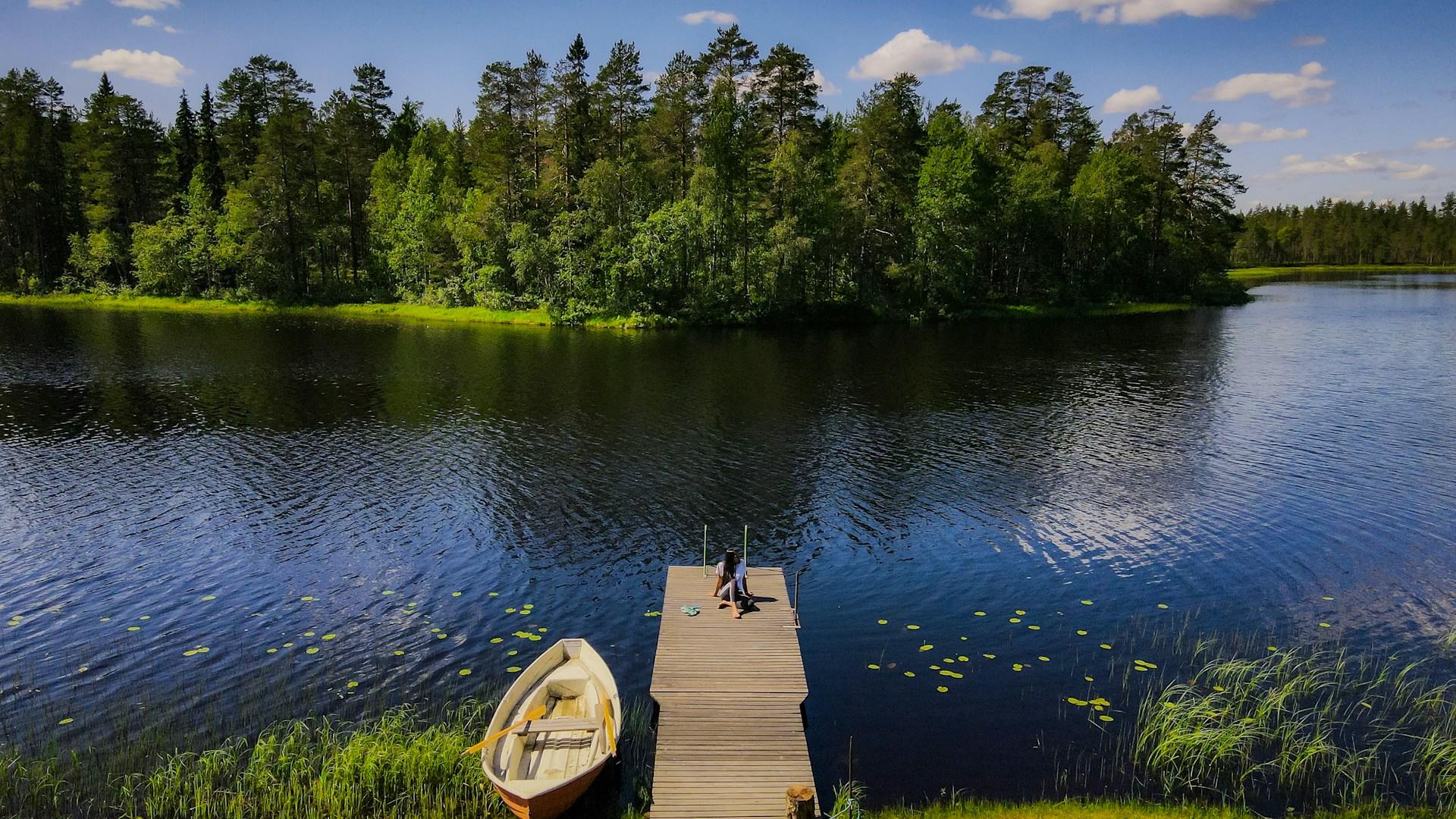 Nainen istumassa laiturilla järvimaisemassa