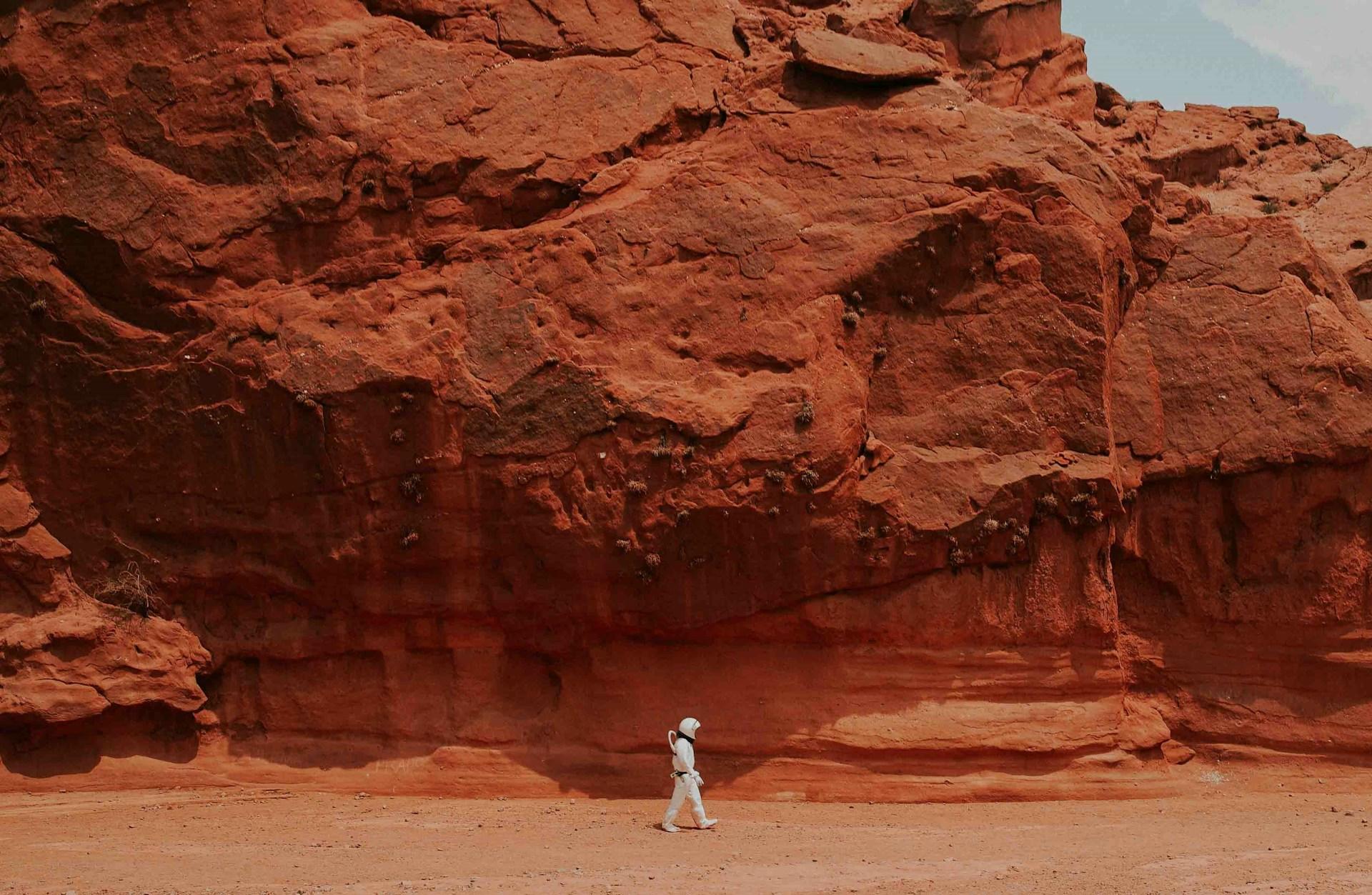 Astronautti kävelemässä punaista kivitaustaa vasten