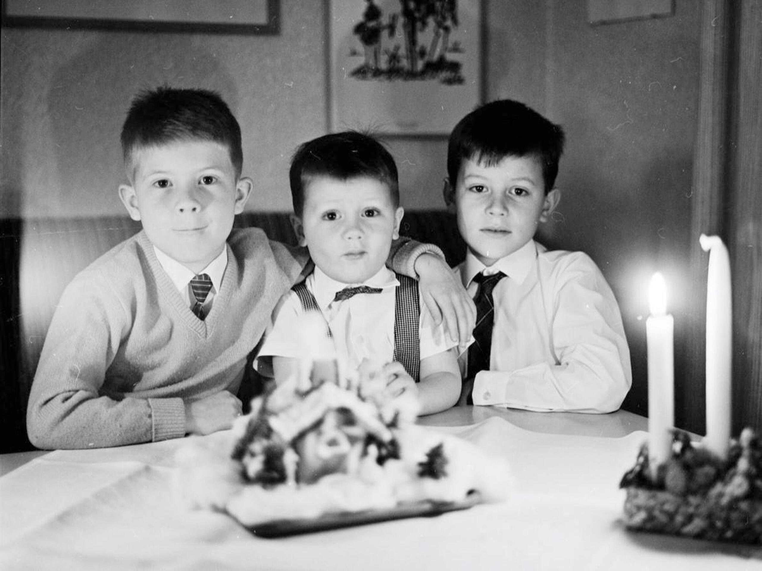 Mustavalkokuva kolmesta pojasta pöydän ääressä