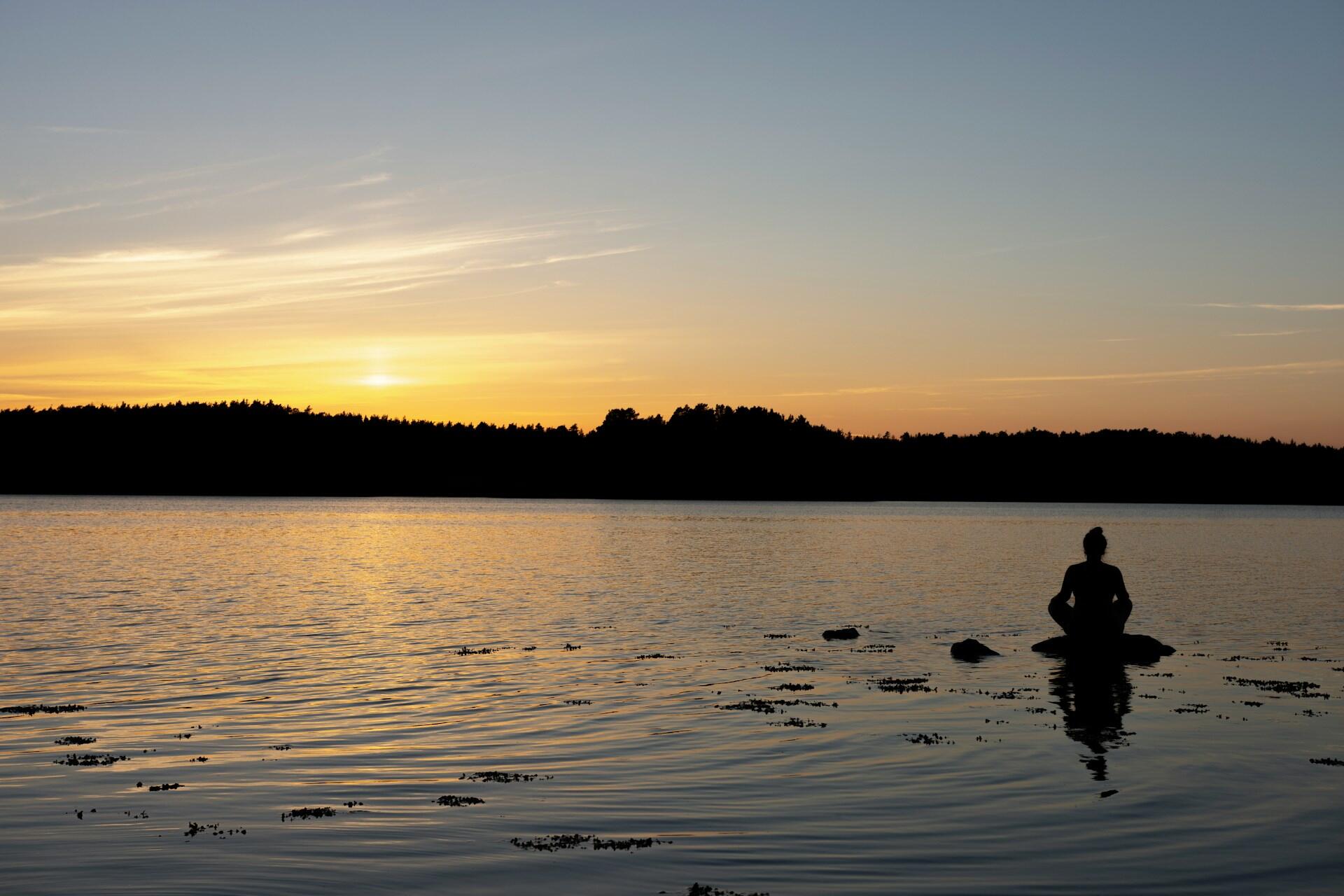 Henkilö istumassa rantakivellä auringonlaskussa