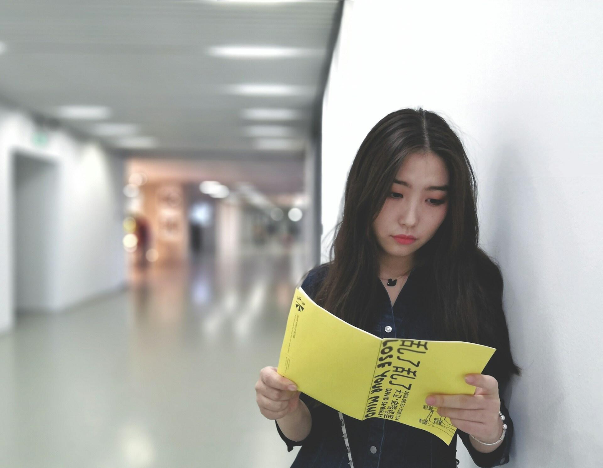 Tummahiuksinen nainen lukemassa keltakansista kirjaa