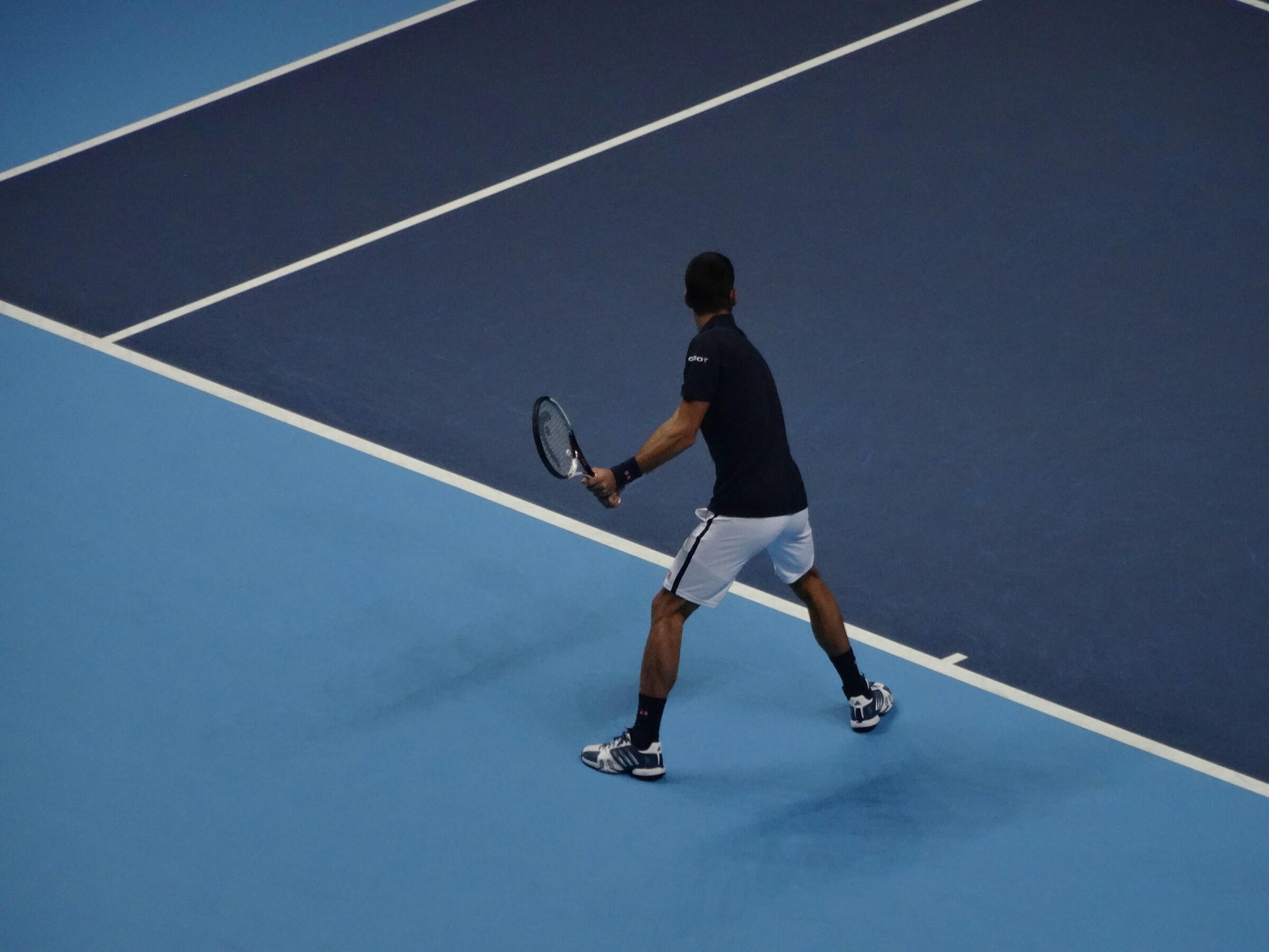 Sininen tenniskenttä ja pelaaja tekemässä syöttöä