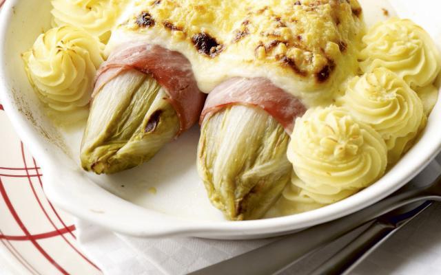 Witlof in hesp gerold op een bord met aardappels en kaas