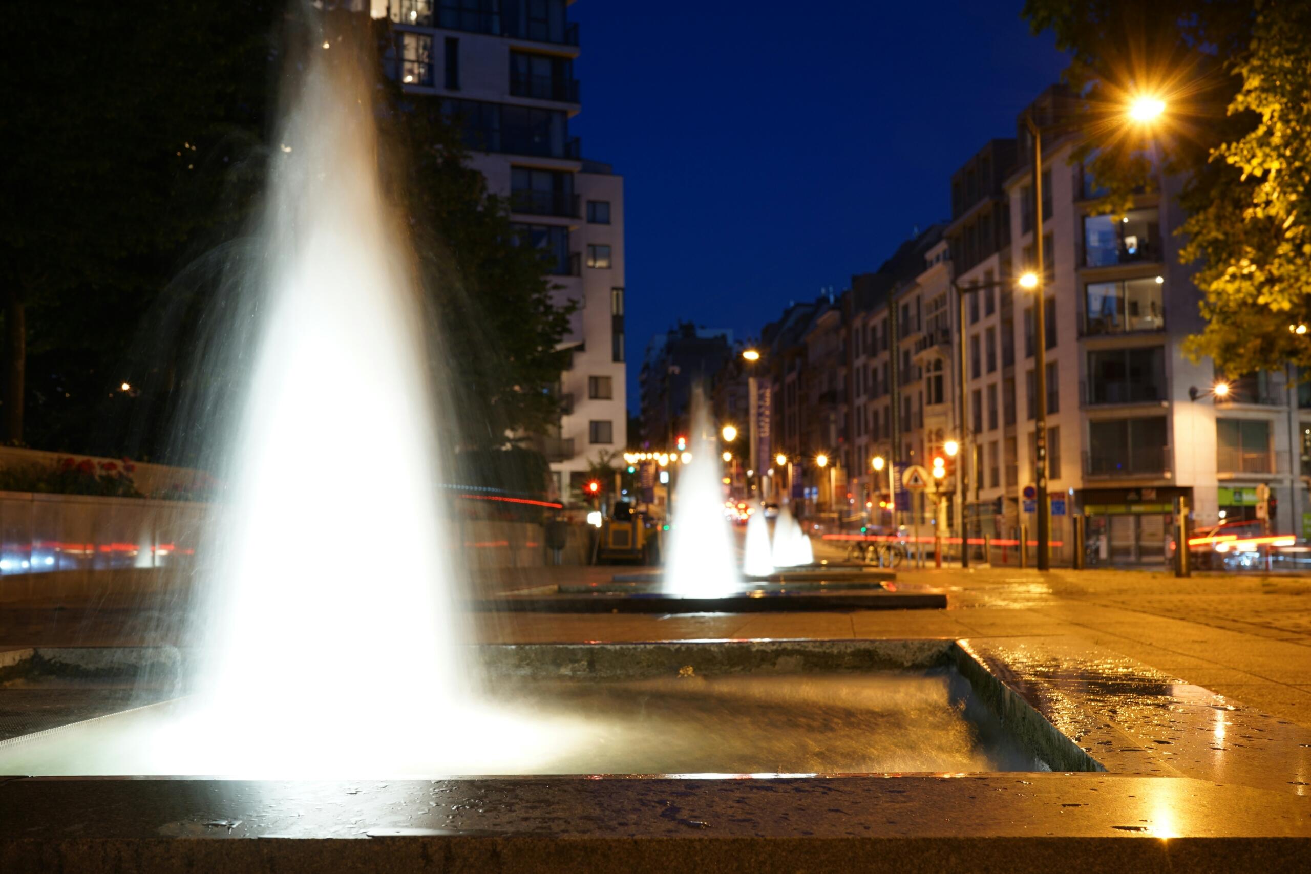 Straat in Brussel bij nacht met verlichte fonteinen en filmische sfeer | Henri Buenen, via Unsplash