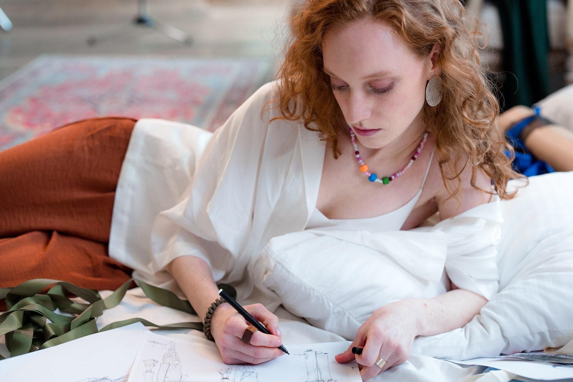 Vrouw tekent kleding op papier terwijl ze op de grond ligt