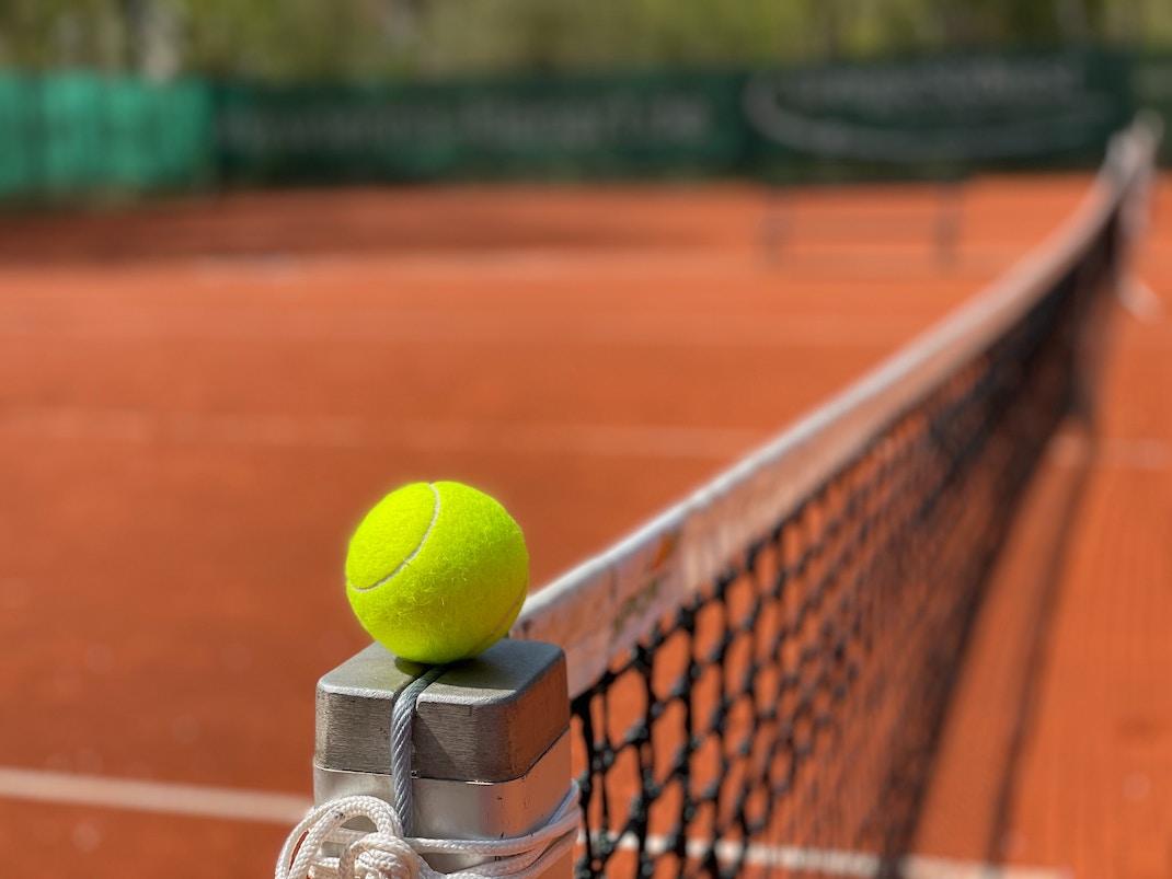 tennisbal naast net op gravelgrond
