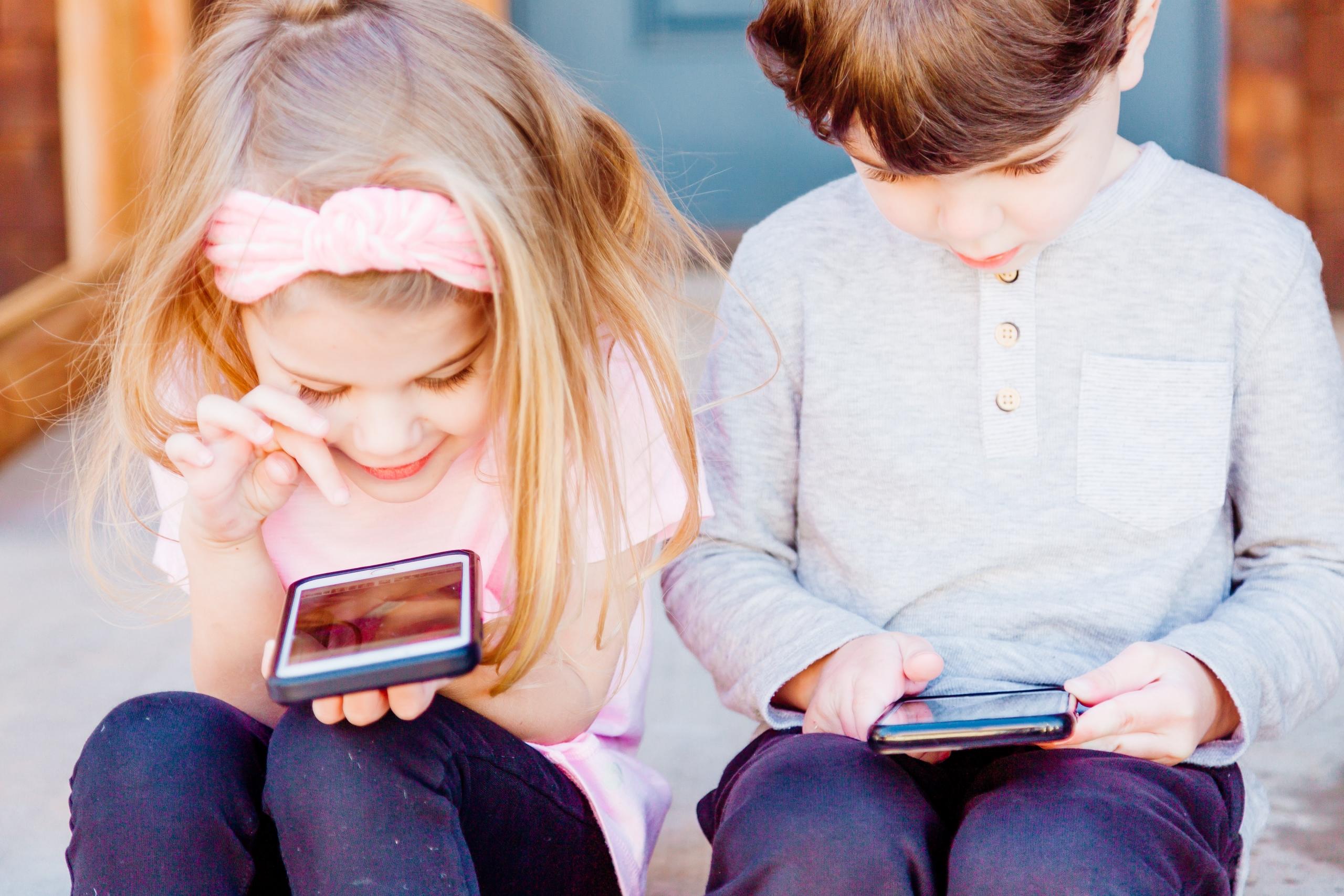 Kinderen zitten naast elkaar en gebruiken telefoons