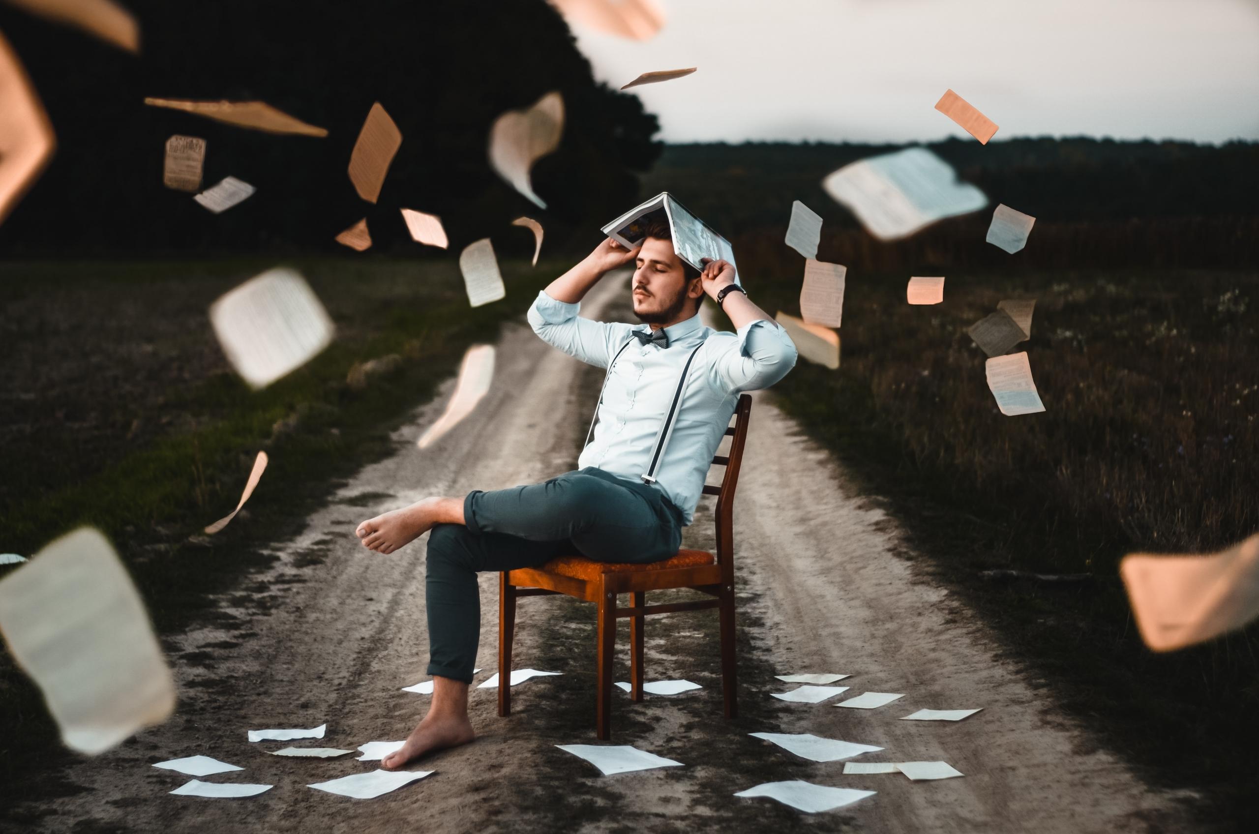 Man op stoel met vallende boeken rond hem