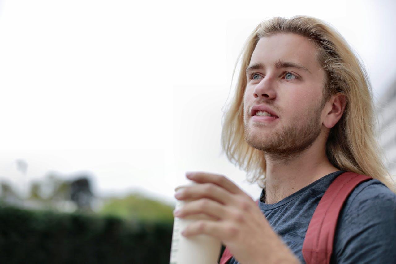jeune homme blond dehors avec un gobelet et un sac a dos rouge