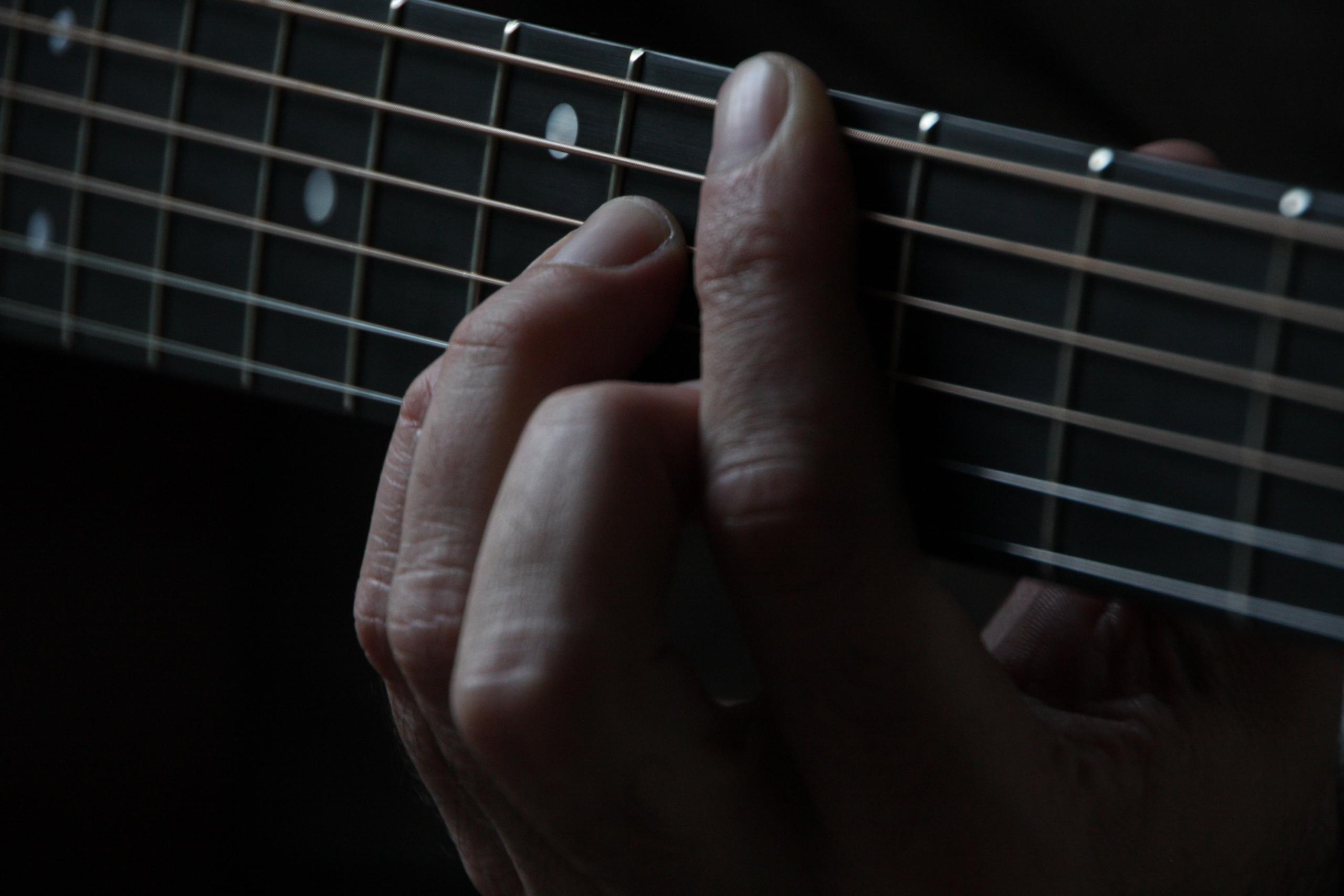 Des mains grattent des cordes de guitare électrique