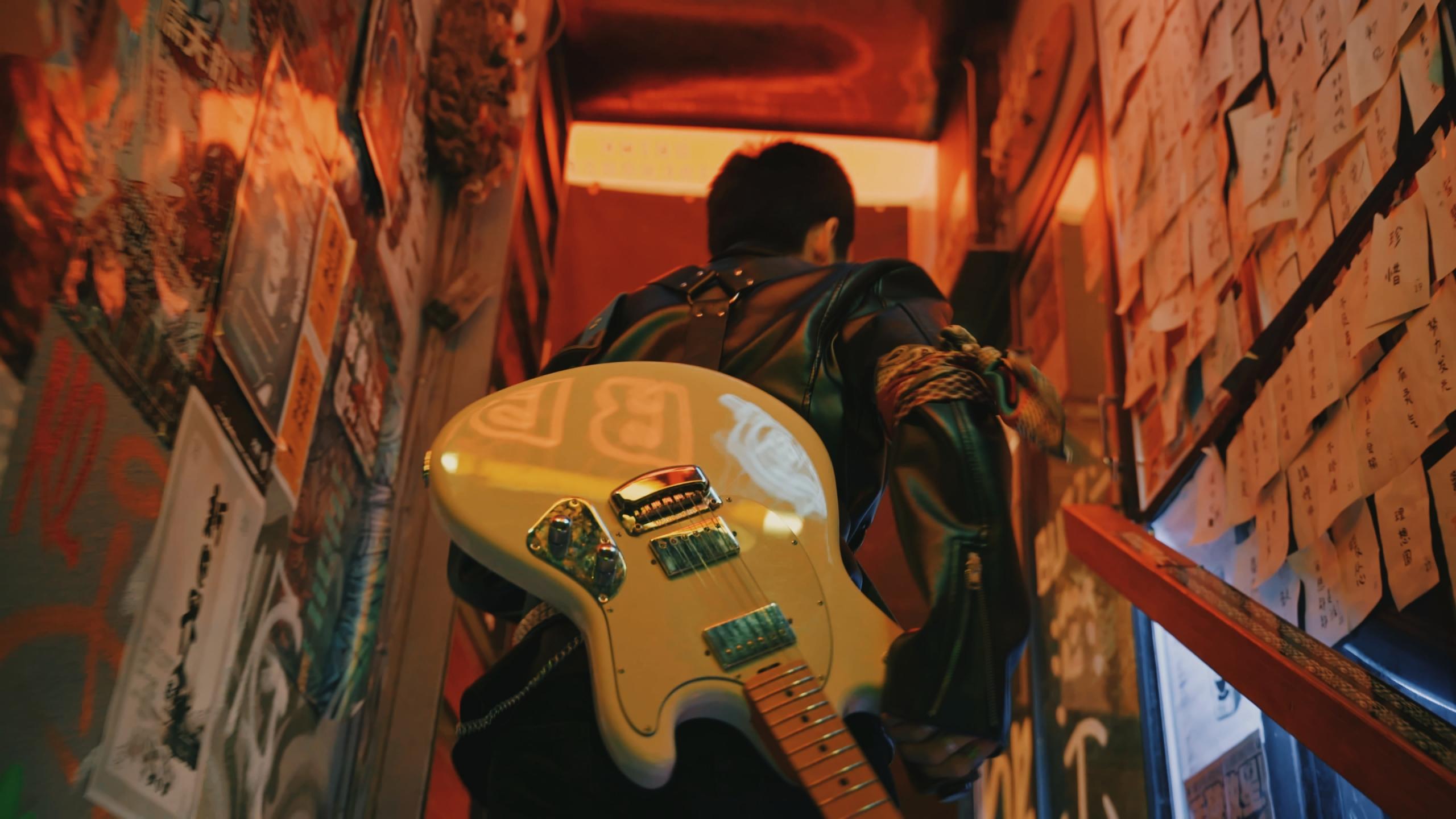 Un guitariste monte des escaliers, sa guitare électrique dans le dos