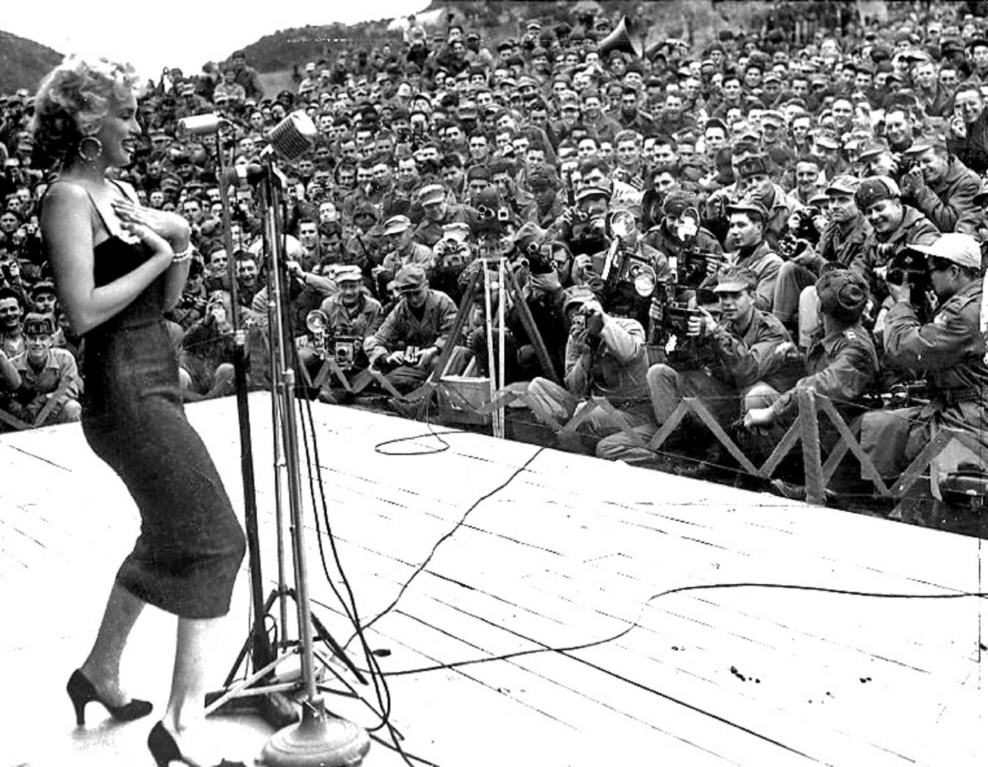 Photo de Marylin Monroe sur scène devant plein de photographes. 