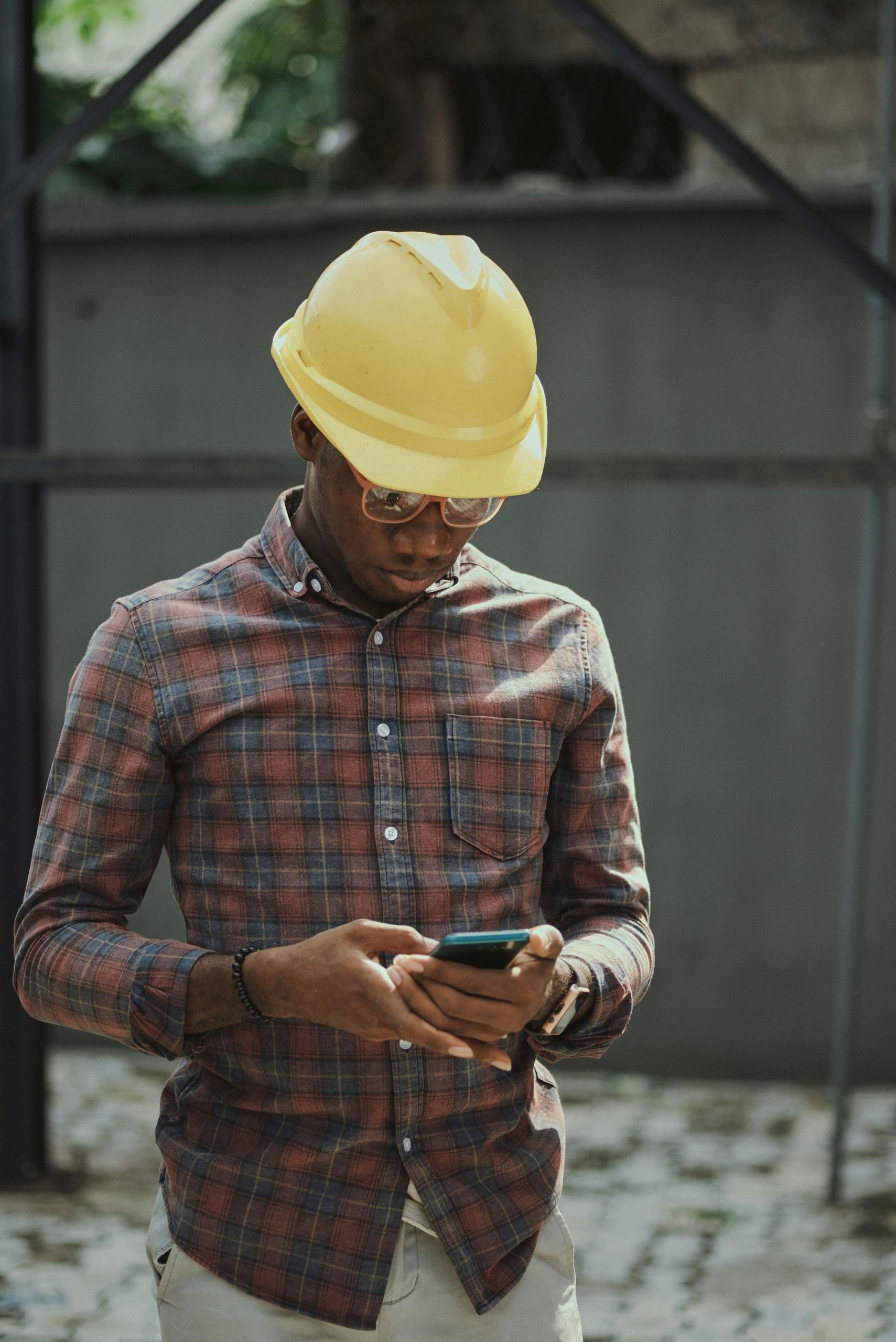Un ouvrier en casque regarde son téléphone.