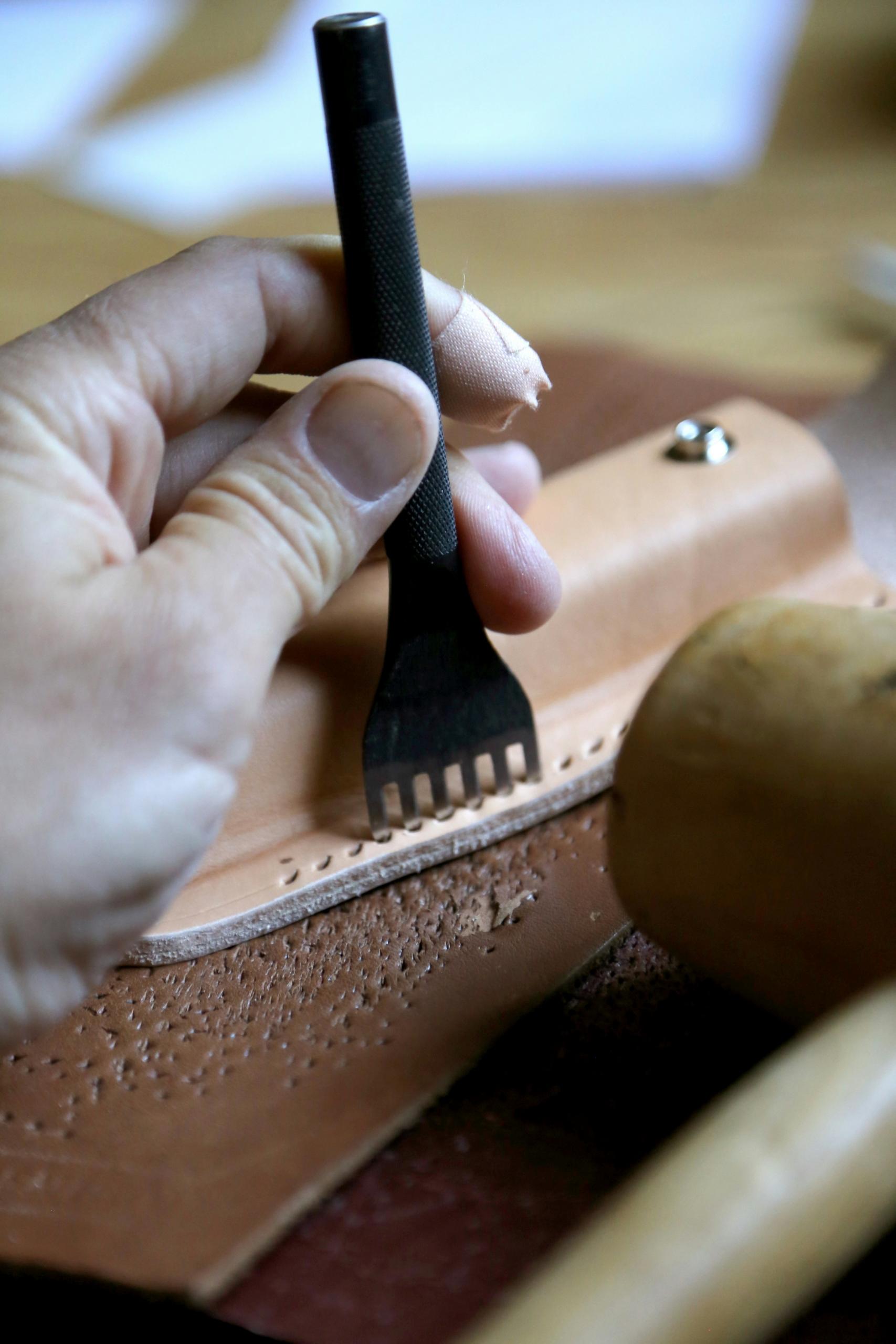 Des mains travaillent une pièce en cuir.