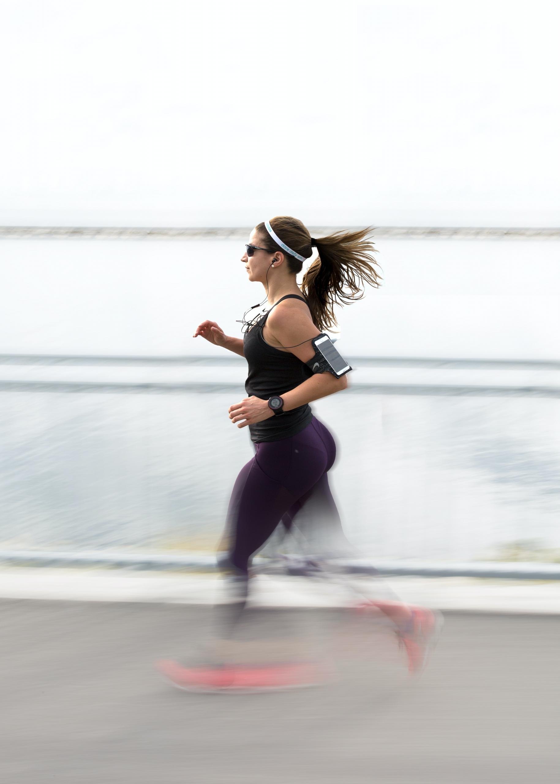 Une femme court avec son téléphone et son app de running accrochée au bras.