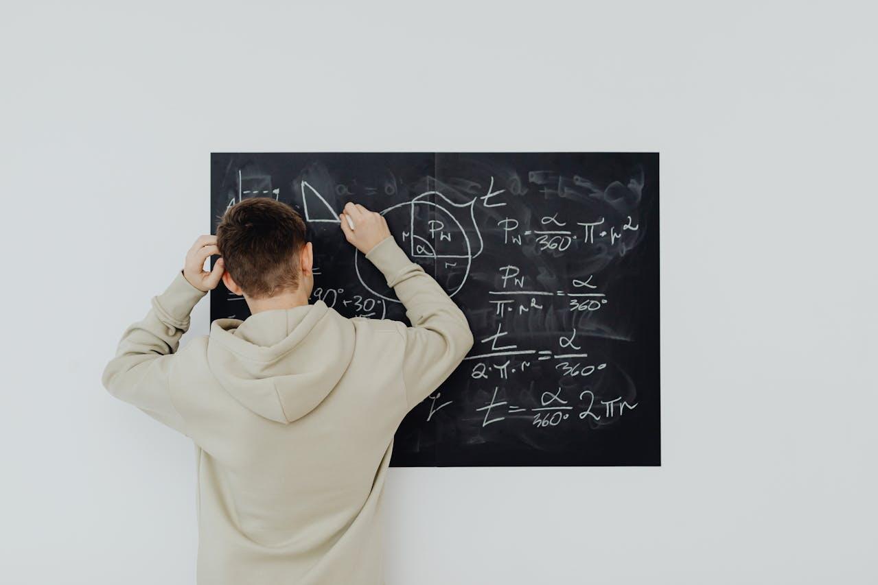 Jeune homme de dos en train d'écrire des formules mathématiques sur un tableau noir.