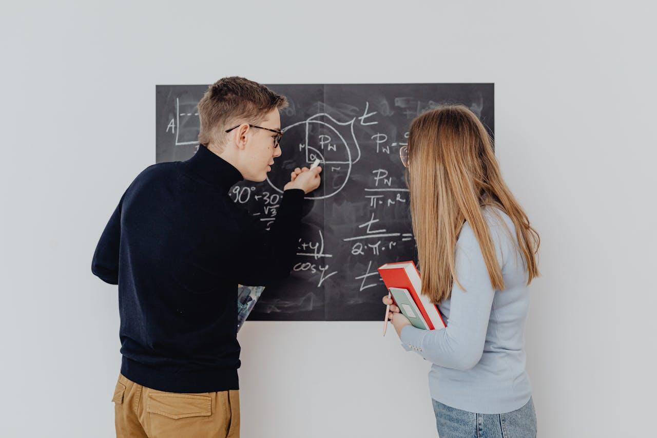 Un jeune homme et une jeune fille se tiennent devant un tableau noir et écrivent des formules mathématiques. 