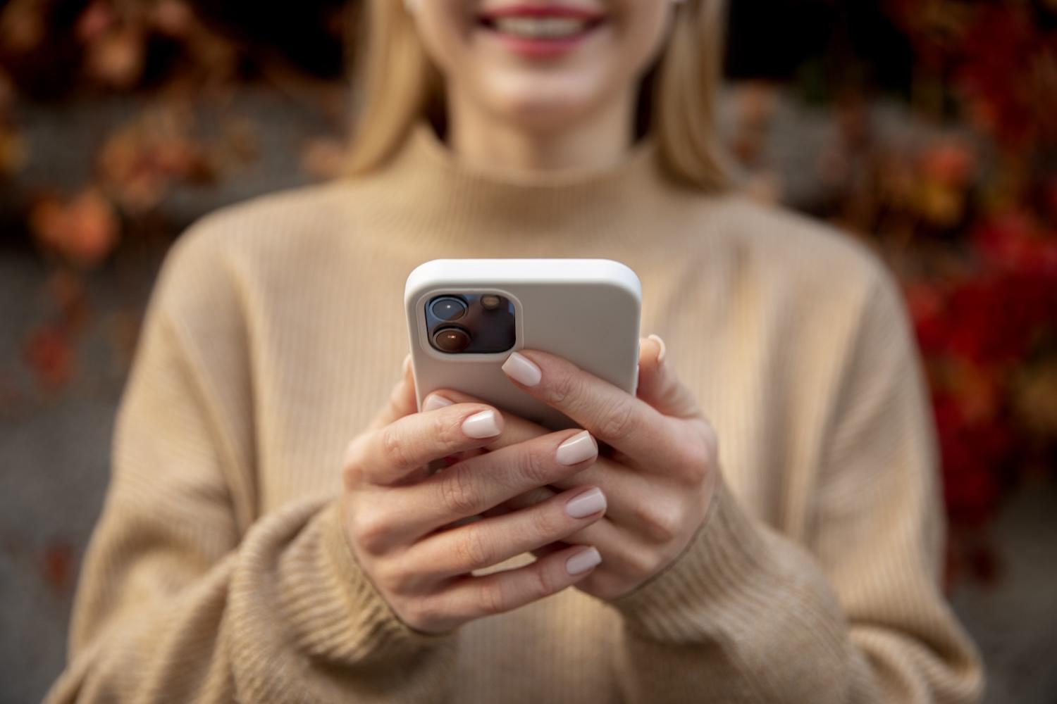 Une jeune femme souriante tient son téléphone devant elle.