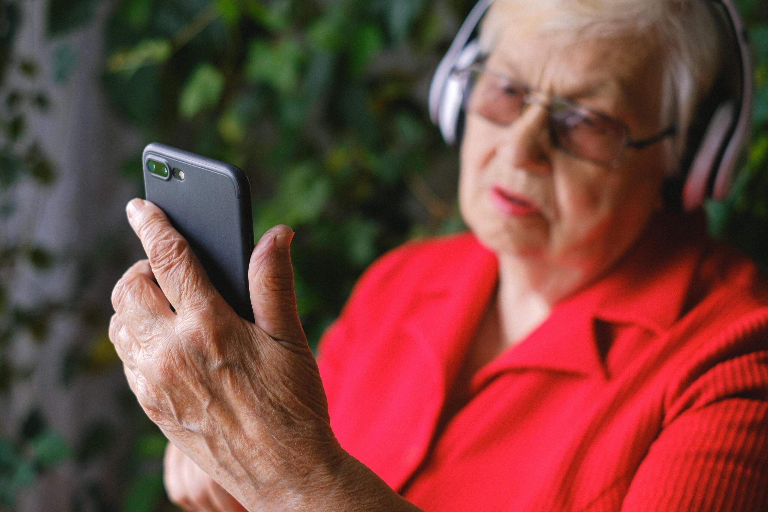 Grand-mère avec un smartphone dans les mains et un casque pour écouter de la musique sur la tête. 