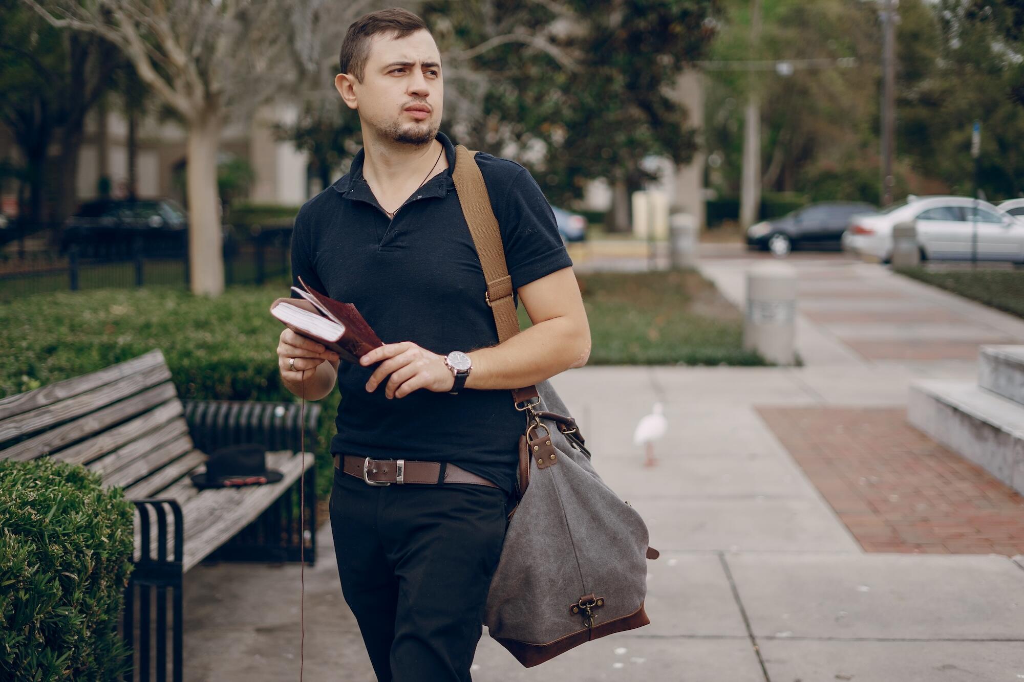 Un jeune homme en tenue sobre porte un sac et des cahiers