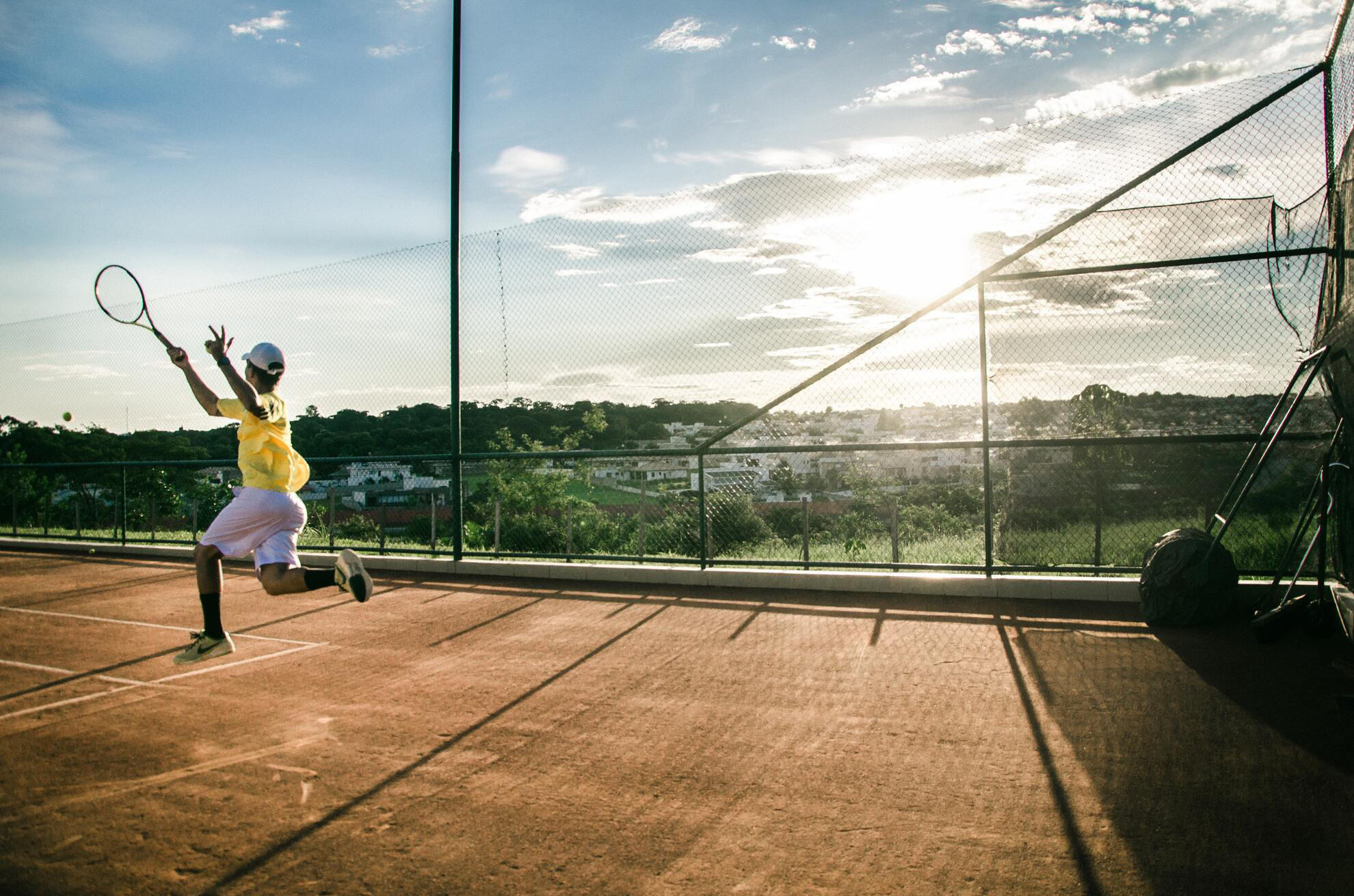 Jeune homme de dos frappant la balle en revers sur un court de tennis en terre battue.