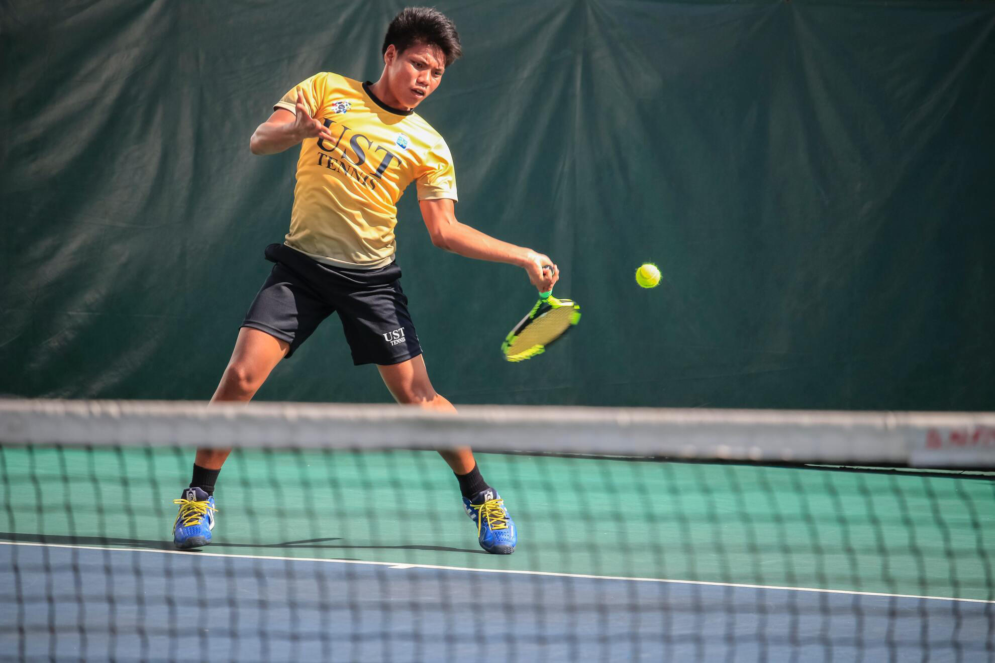 Jeune homme asiatique frappant en coup droit dans une balle de tennis sur un court en surface dure.