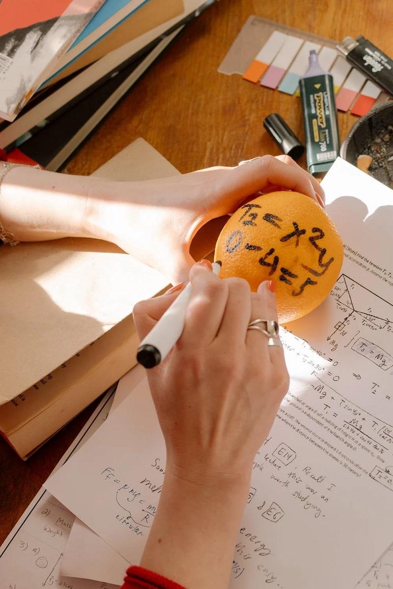 Une personne réalise une opération mathématiques sur une orange. 