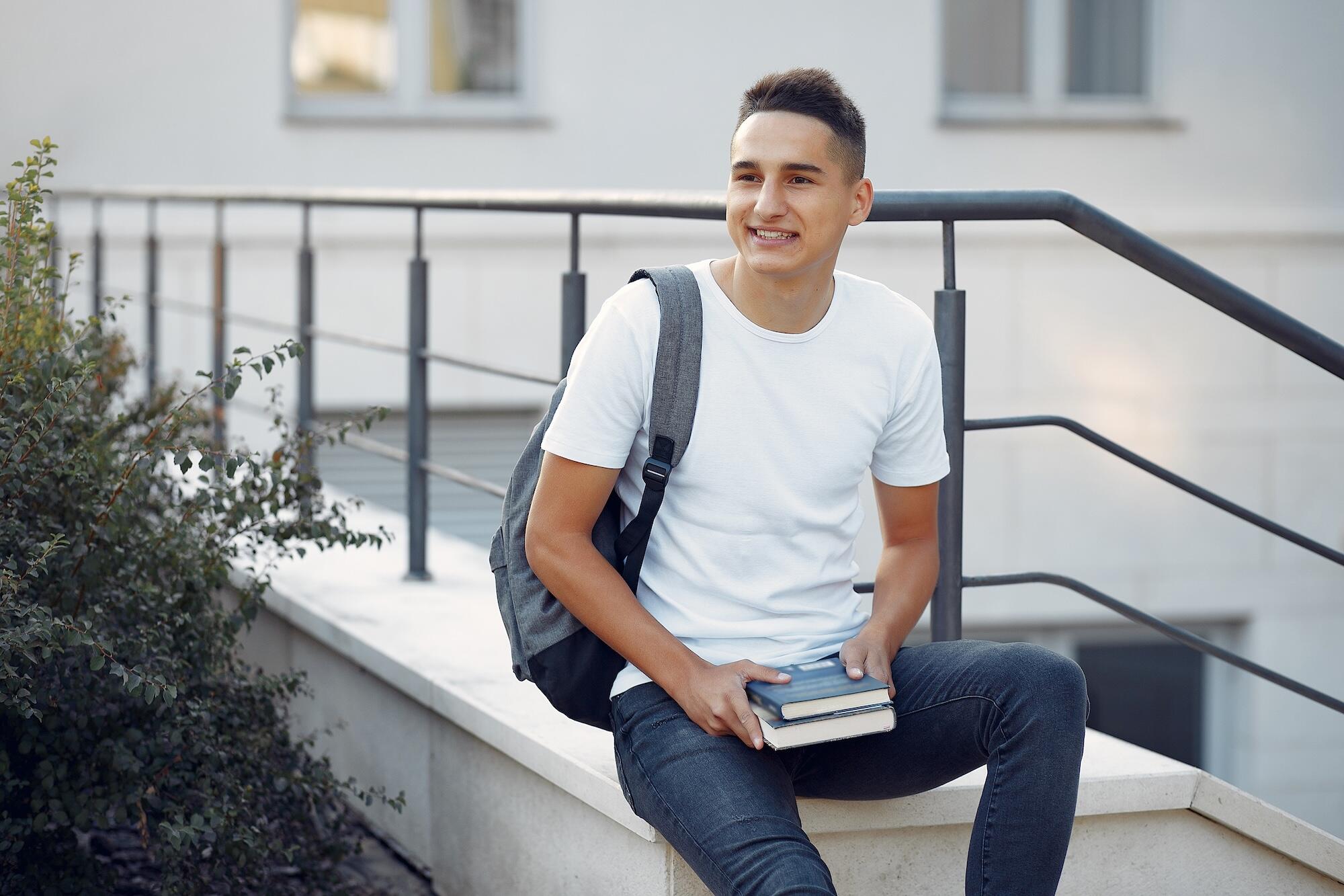 Jeune homme avec un t-shirt blanc assis sur un muret
