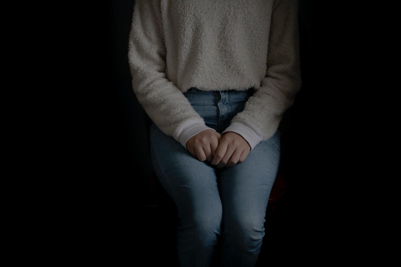 Jeune femme assise dans le noir, les mains sur les genoux, semblant anxieuse.