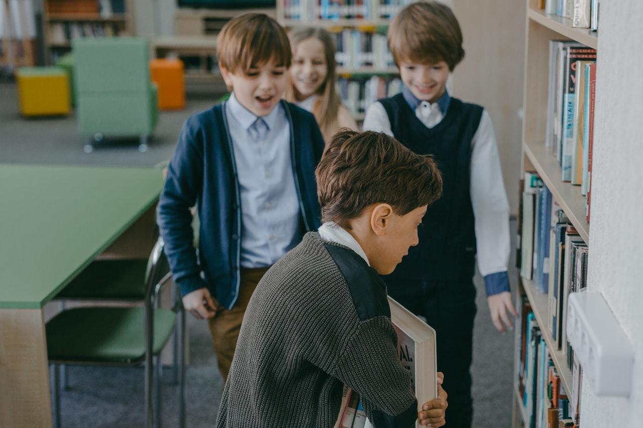 Jeunes garçons embêtant un camarade de classe dans la bibliothèque.