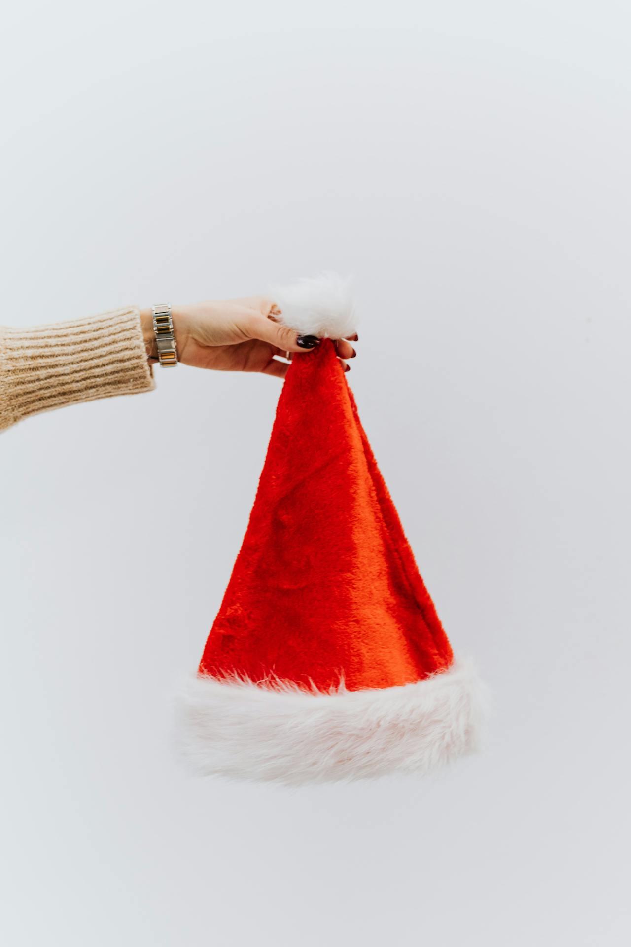 Un bonnet de Noël tenu par le pompon par une main féminine. 