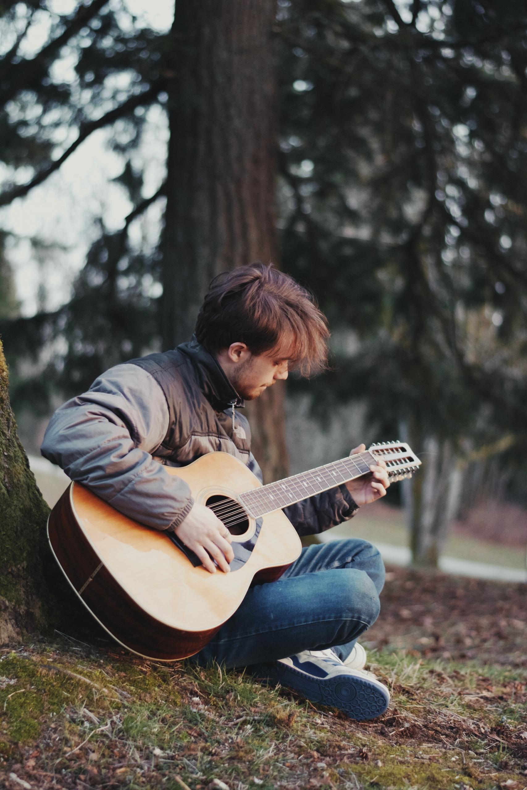 Une jeune homme joue de la guitare en forêt.