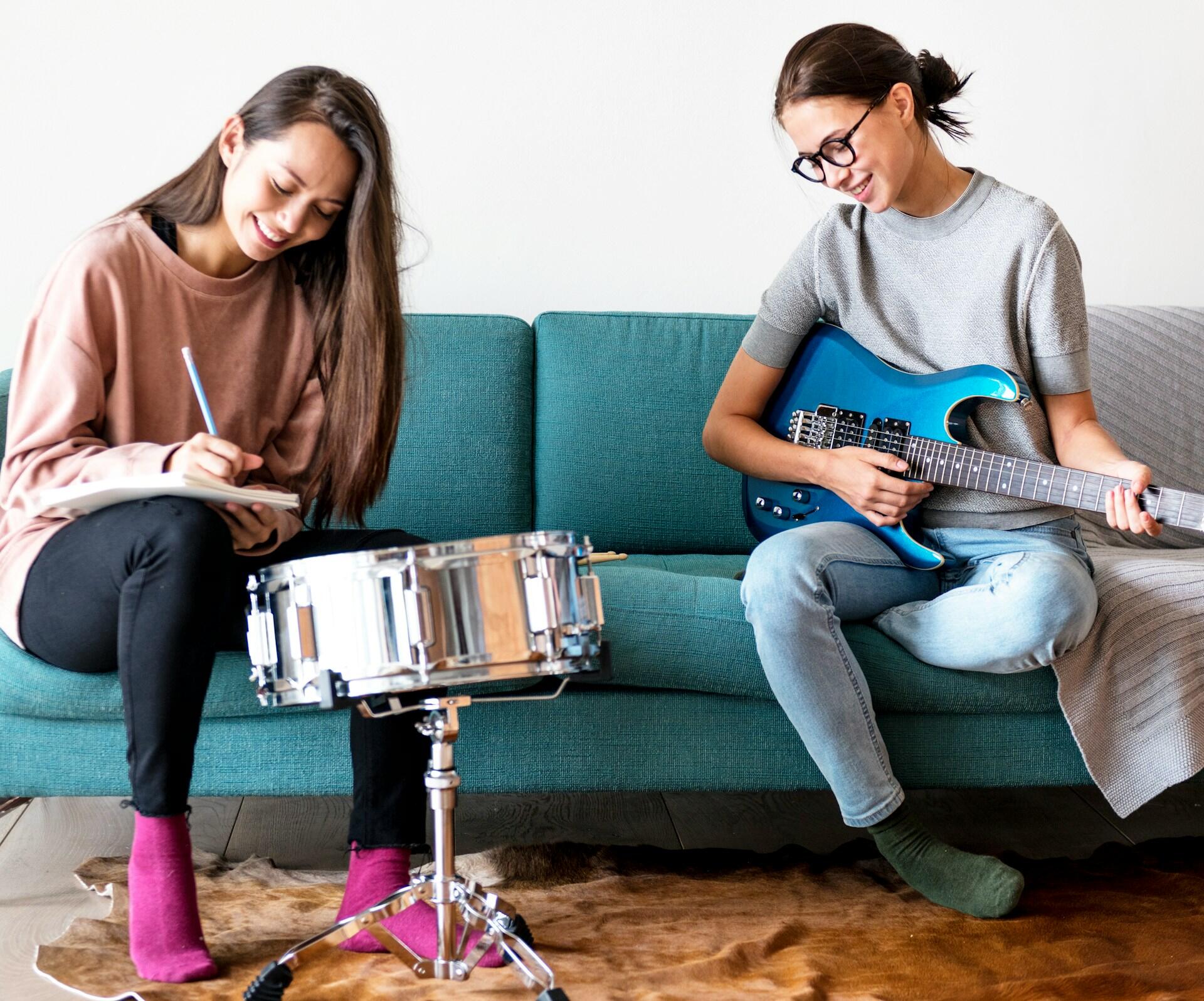 Deux femmes assises sur un canapé qui jouent à la guitare et prennent des notes