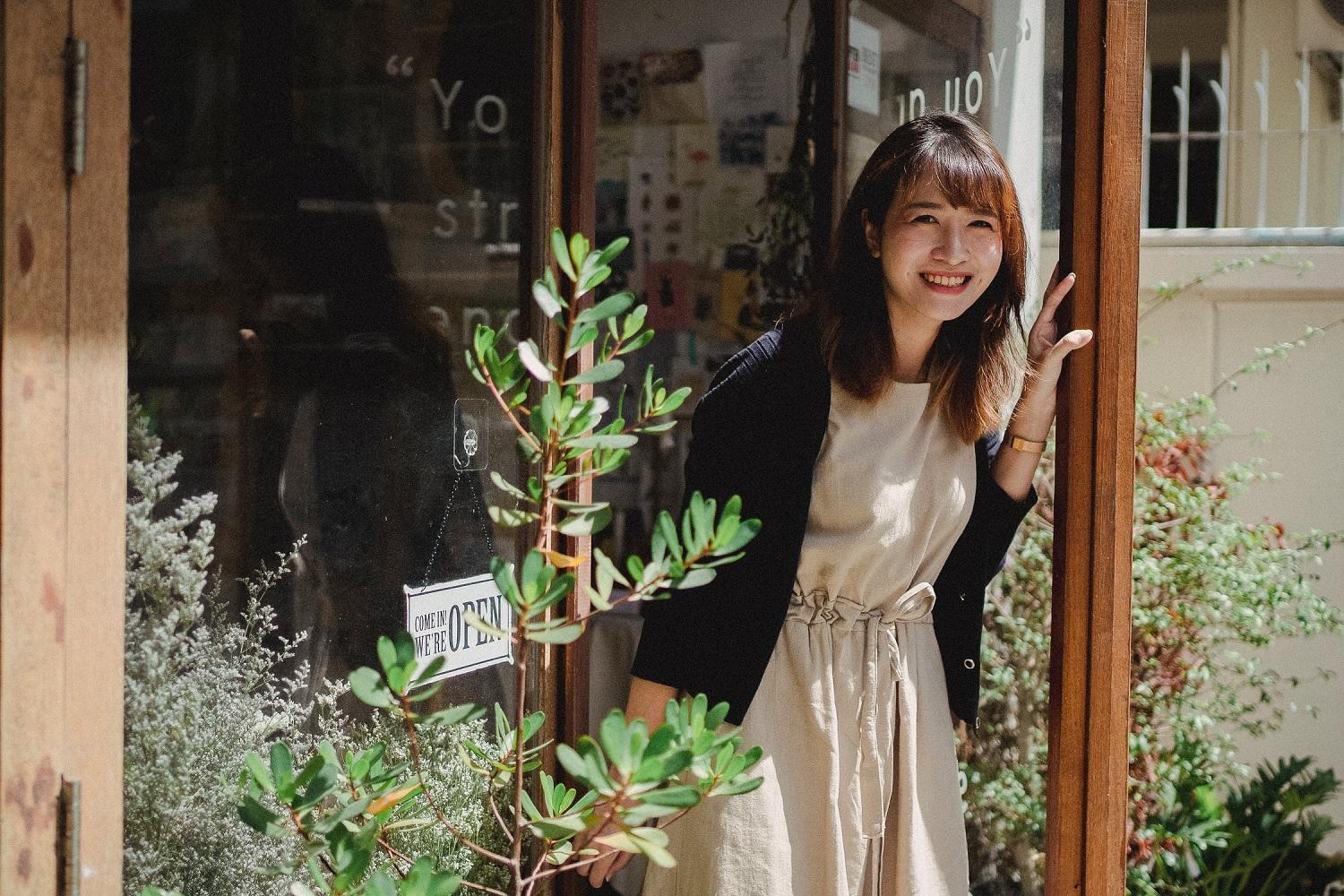 Une apprentie fleuriste se tient devant une boutique.