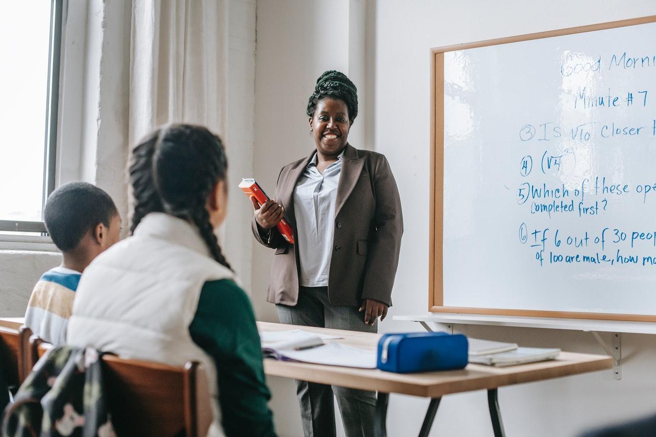 Une maîtresse d'école au tableau donne cours à deux enfants de classe élémentaire.