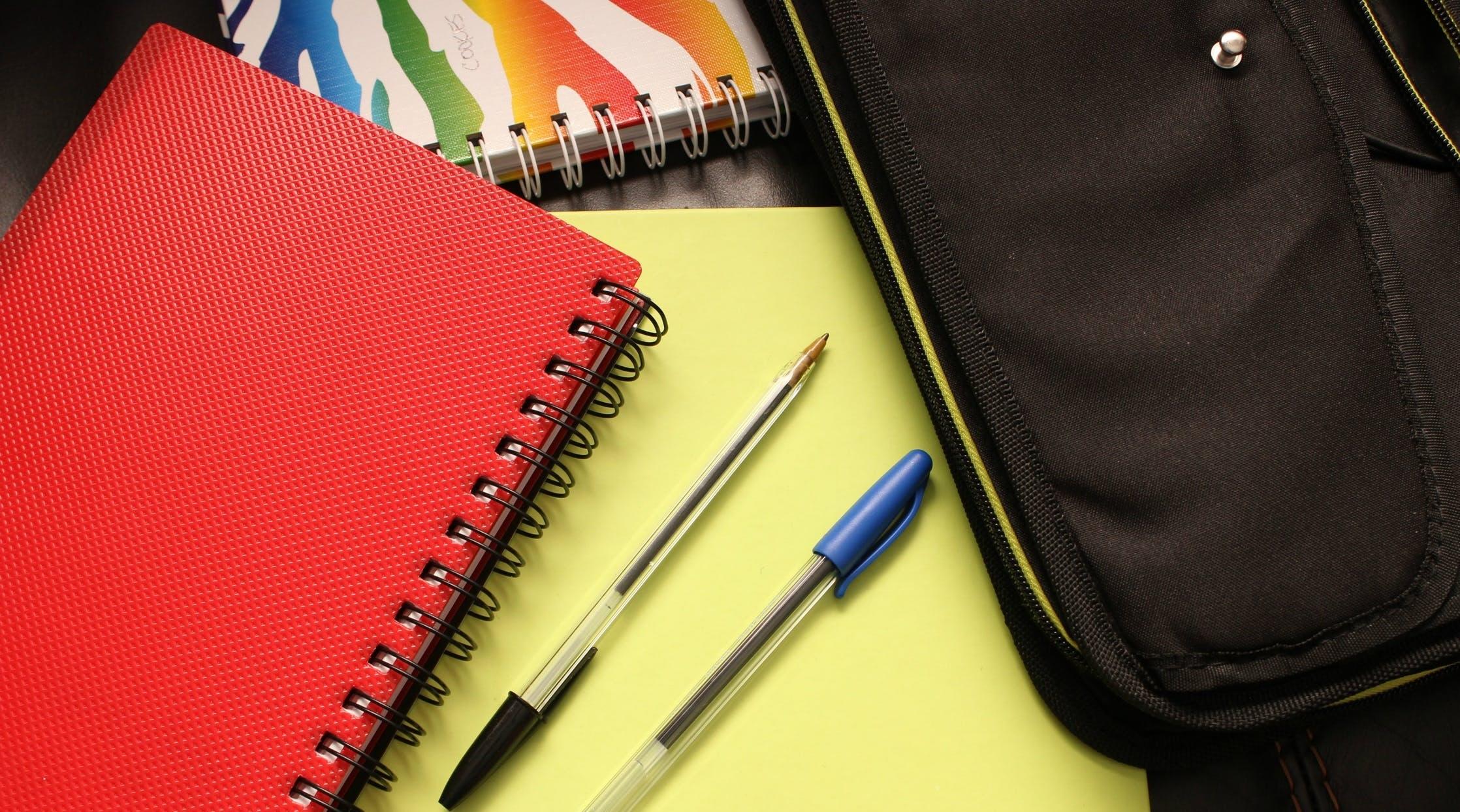 Des cahiers d'apprenti sont étalés avec des stylos.