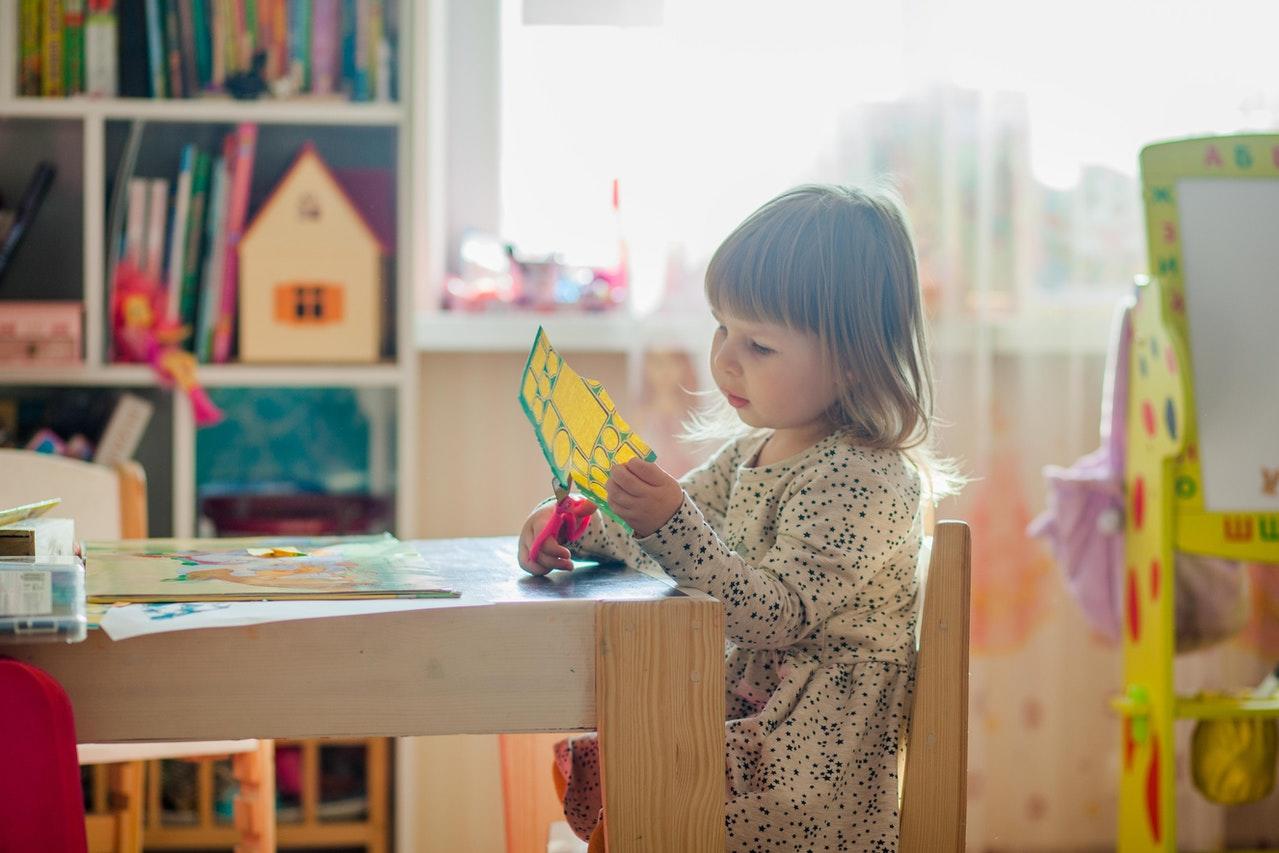 Petite fille dans une classe d'école maternelle découpant des étiquettes à l'aide d'un ciseau.