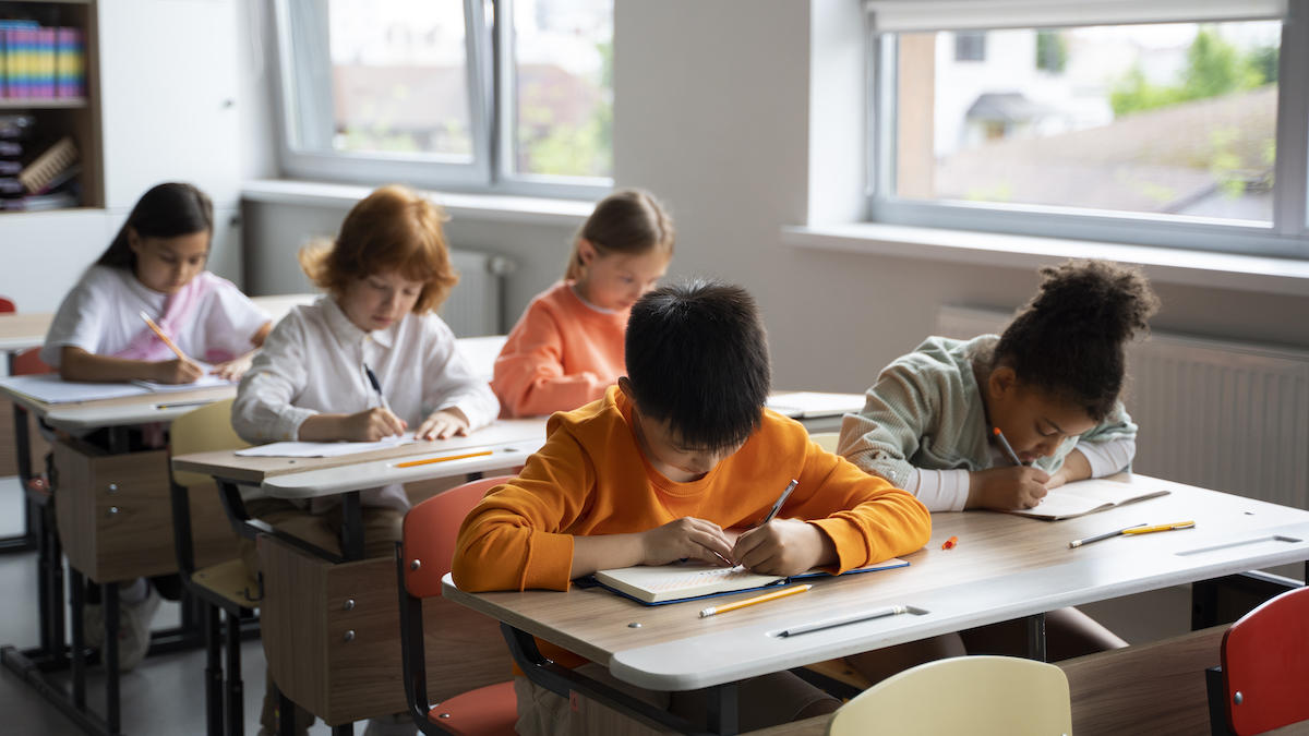 Jeunes élèves en classe en train d'écrire sur leur cahier.