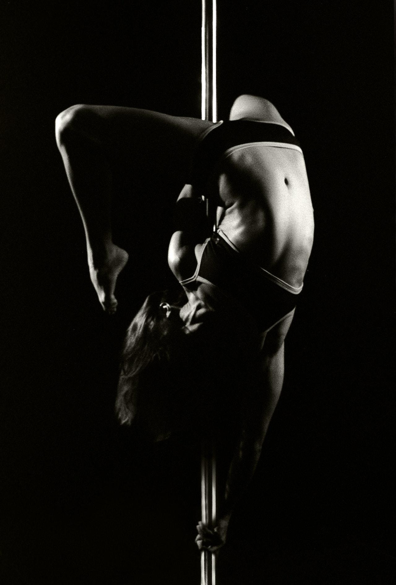 Jeune femme tête en bas sur une barre de pole dance.